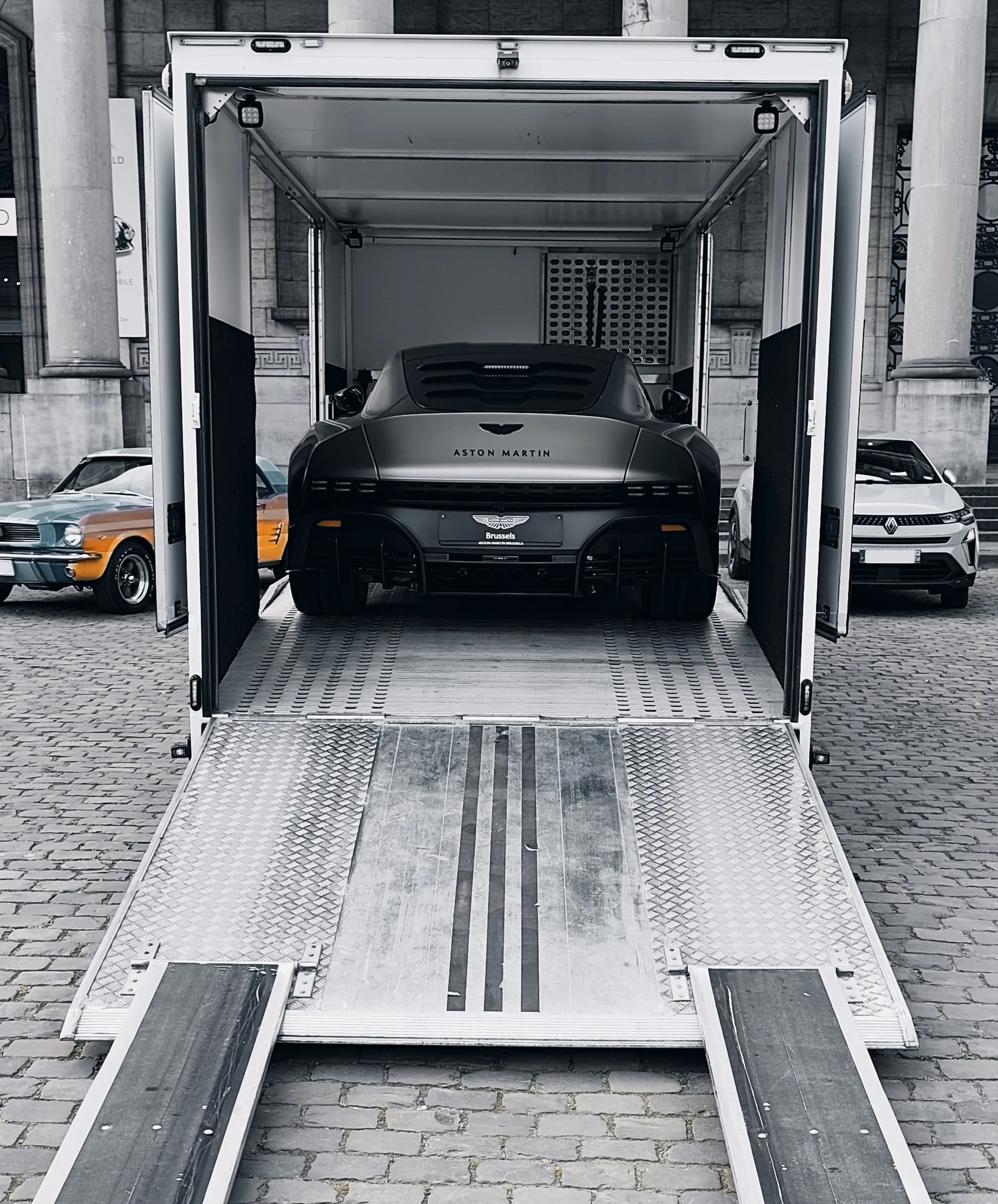 Gesloten transporter met platen neer, Aston Martin Valour aan boord, Brusselse straat