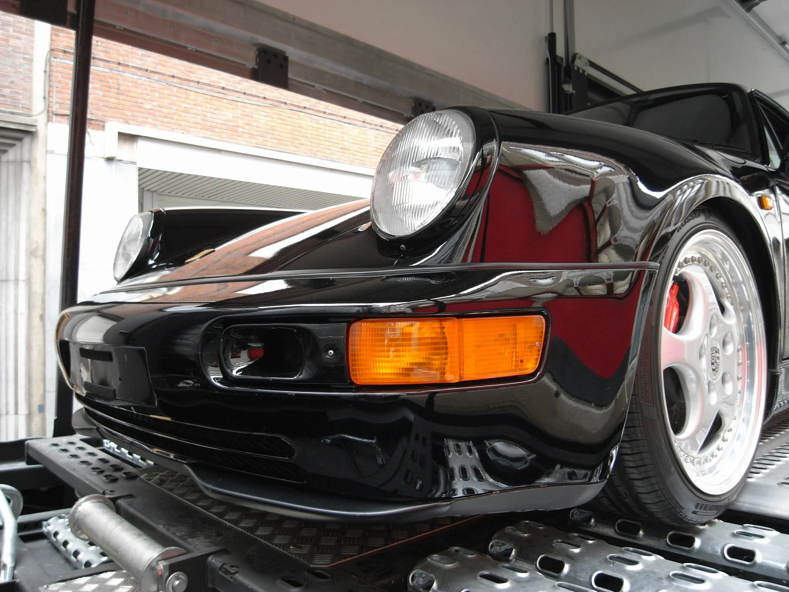 Driekwart vooraanzicht van een zwarte Porsche 911 Turbo met rood interieur in een transporter