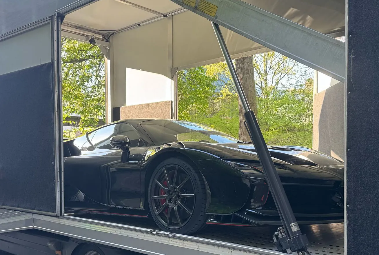 Zwarte hypercar in een gesloten trailer op een private oprit