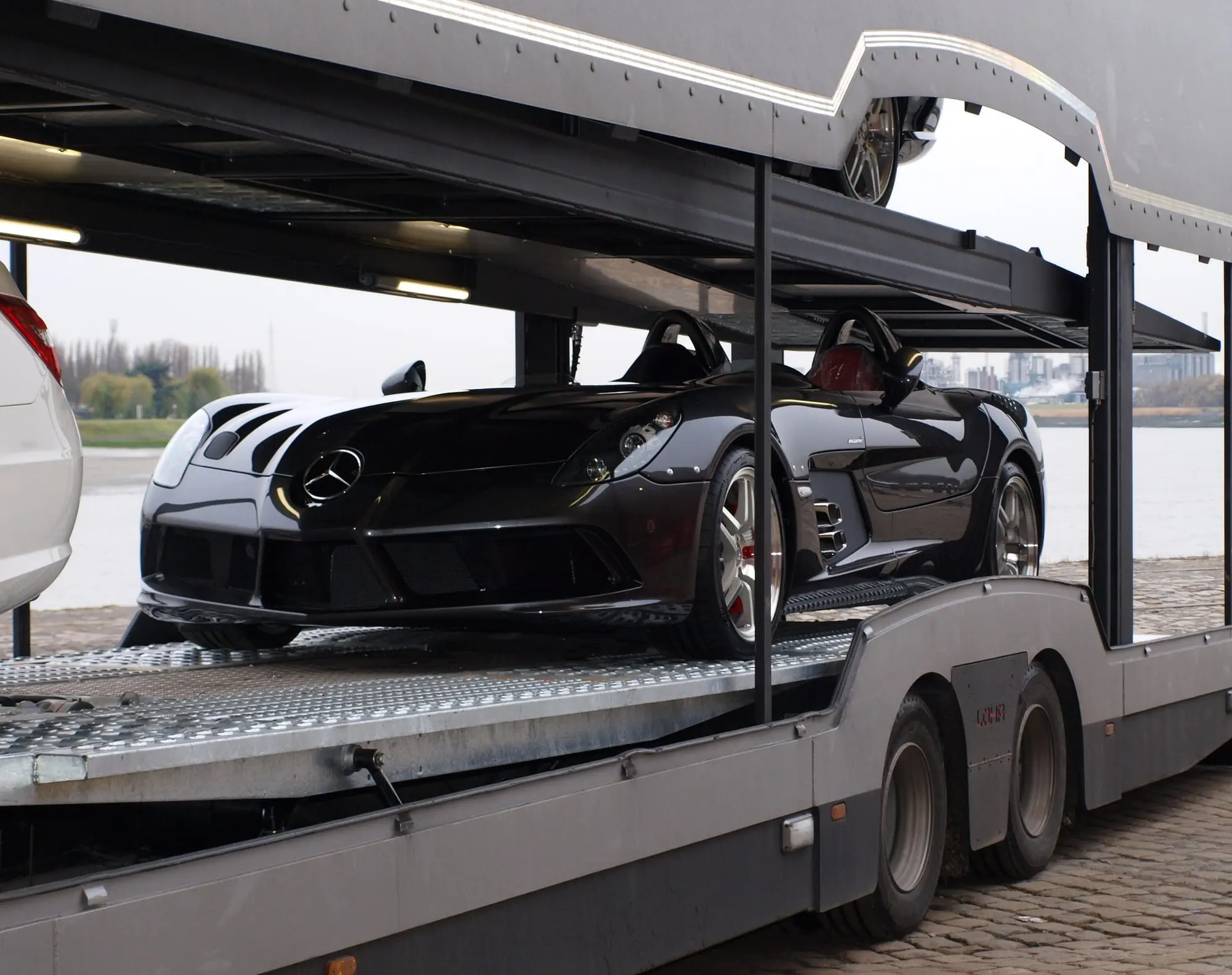 Black Mercedes SLR McLaren on the deck of an e-motion transporter, on the quayside by the water