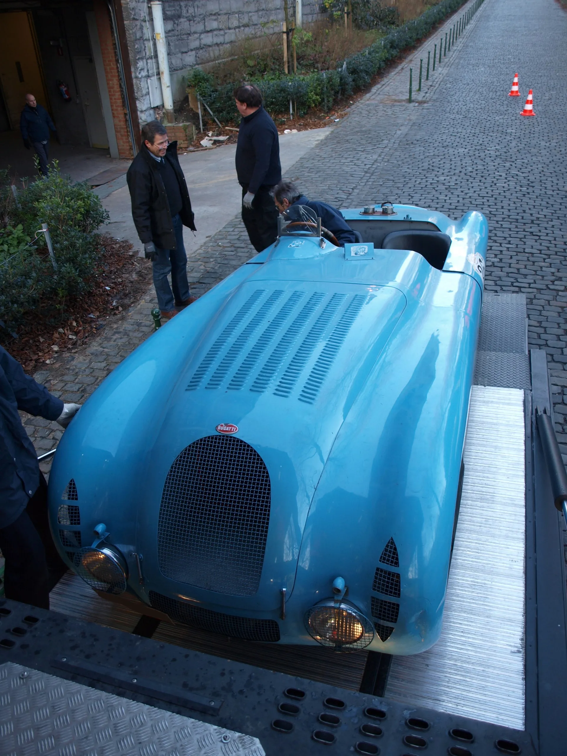 Blauwe gestroomlijnde Bugatti rijdt de platen af in een kasseienstraat