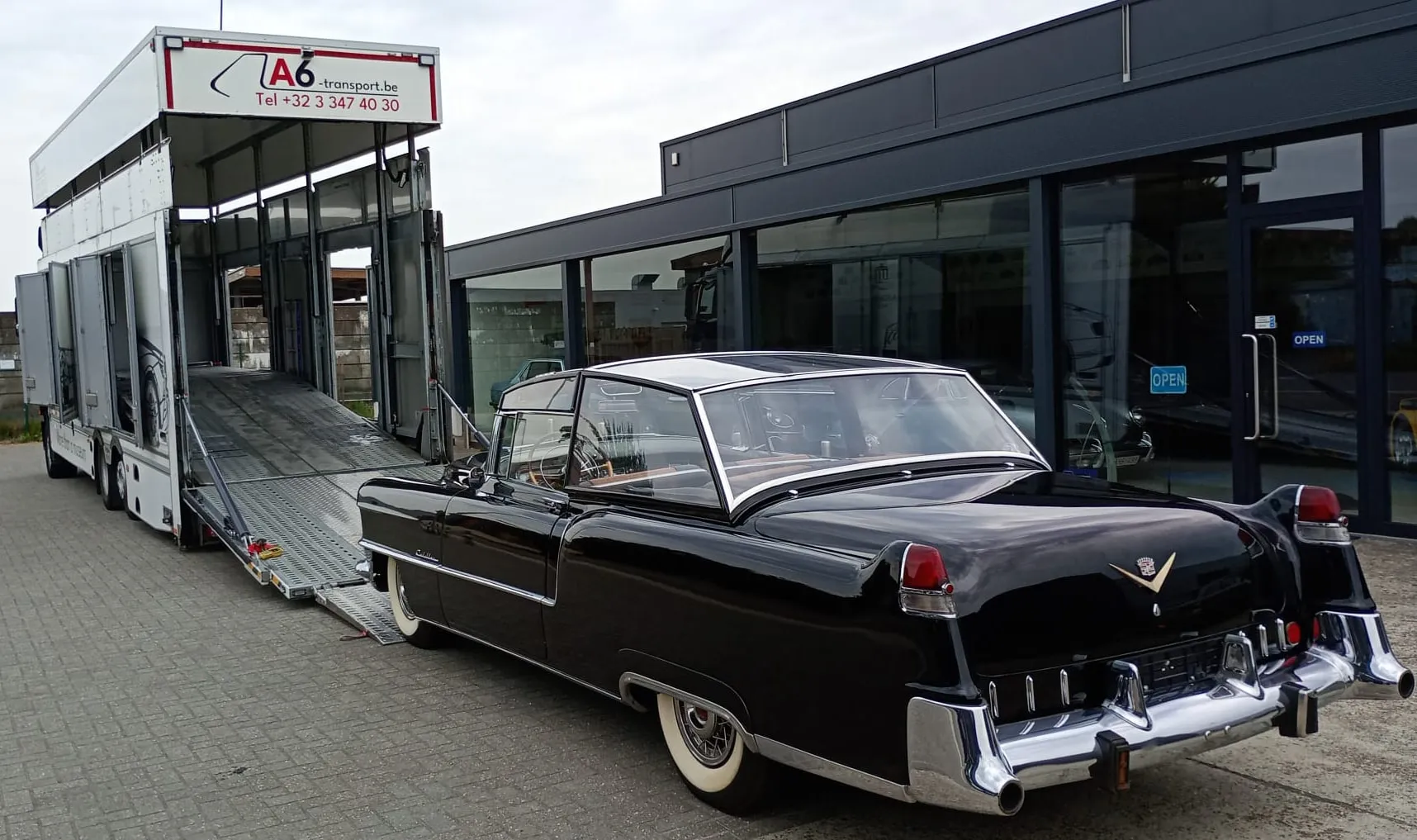 Zwarte Cadillac cabriolet naast een open autotransporter