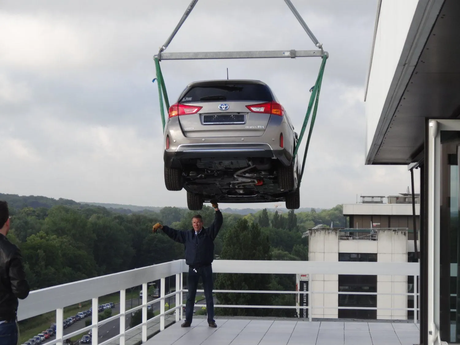 Voiture hissée par grue sur la terrasse d'un immeuble de bureaux, un membre de l'équipe la guide