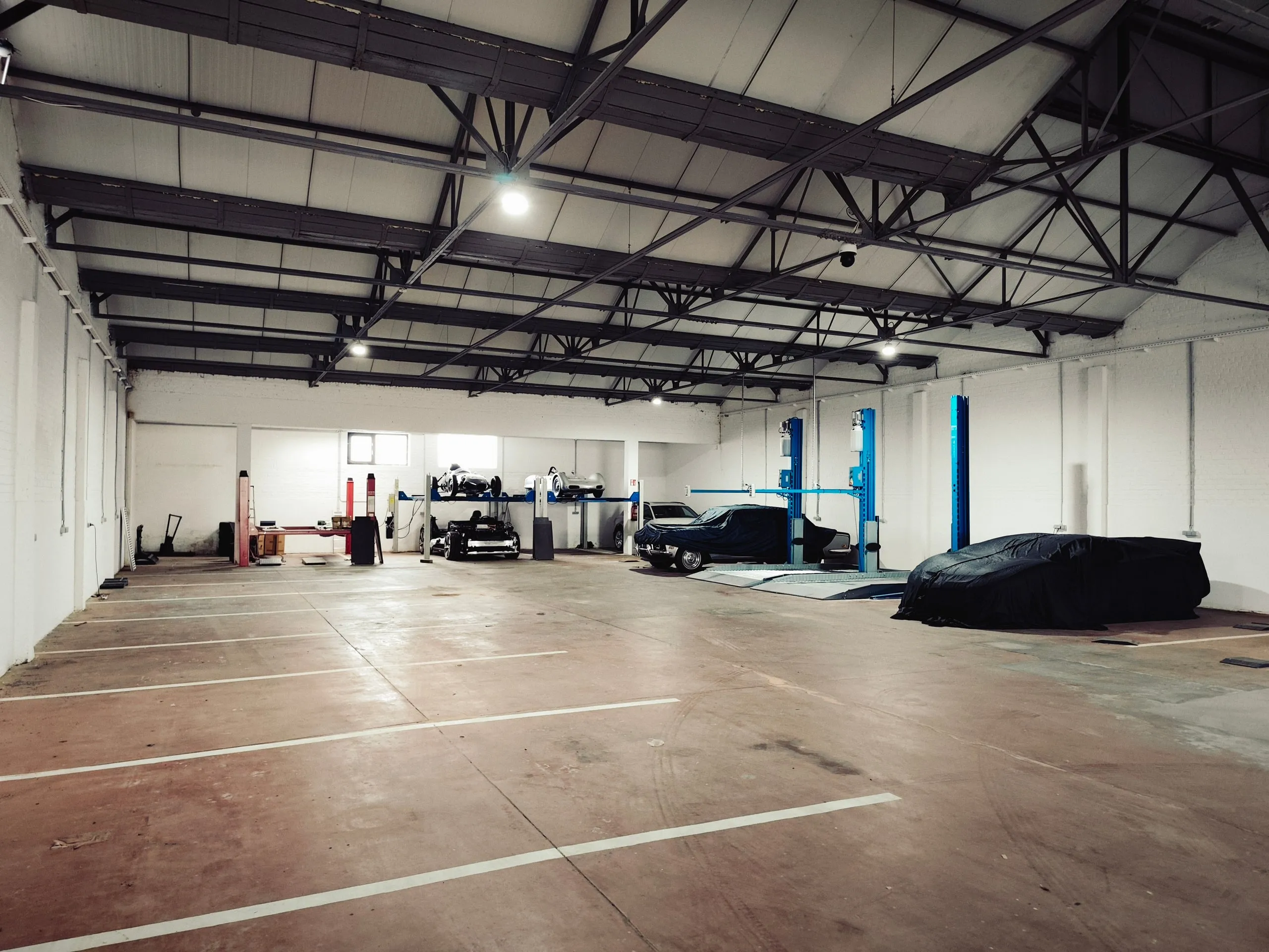 Nave de guardacoches con plazas marcadas en el suelo, coches cubiertos y elevadores al fondo