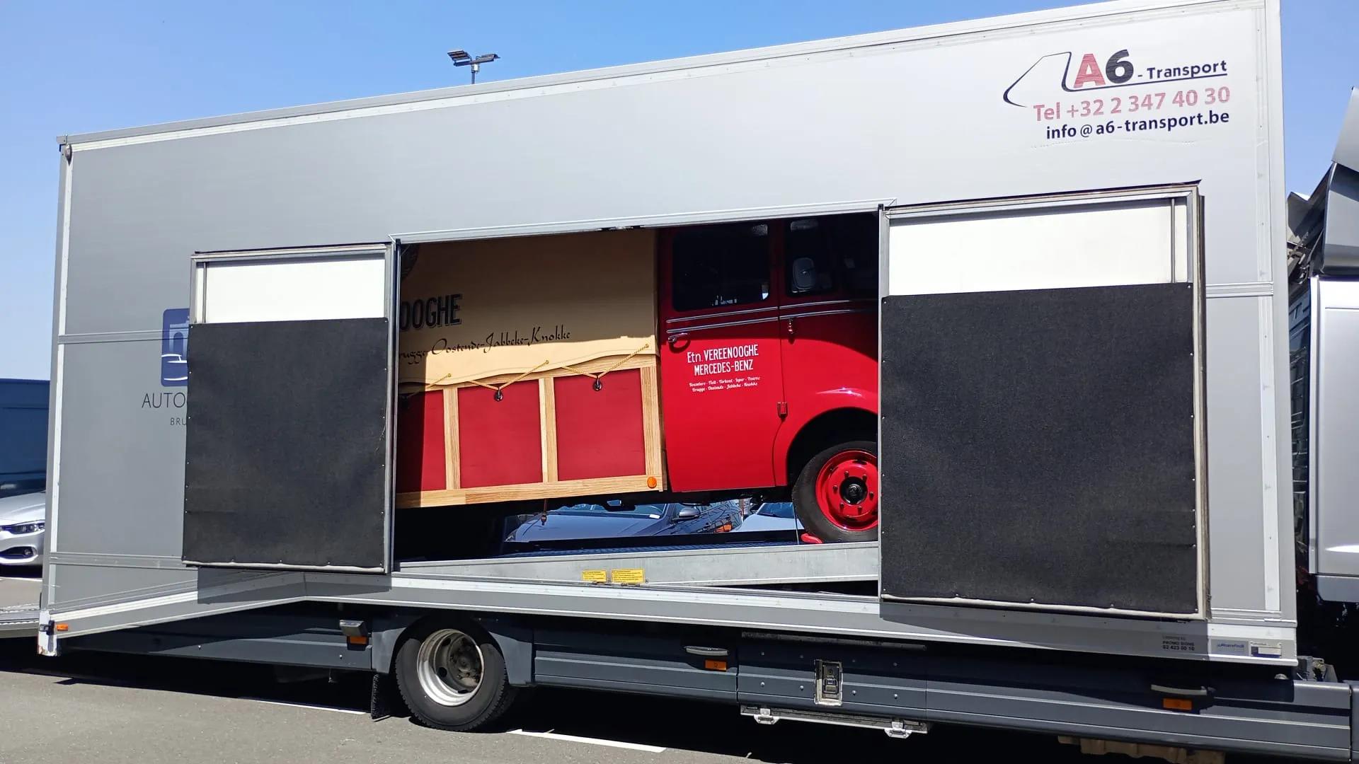 Rode Mercedes-bestelwagen uit de oude doos aan boord van een gesloten transporter