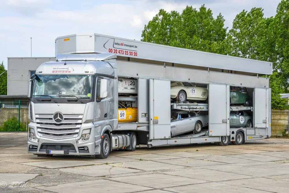 Gesloten transporter met alle zijdeuren open, klassieke racewagens op beide dekken