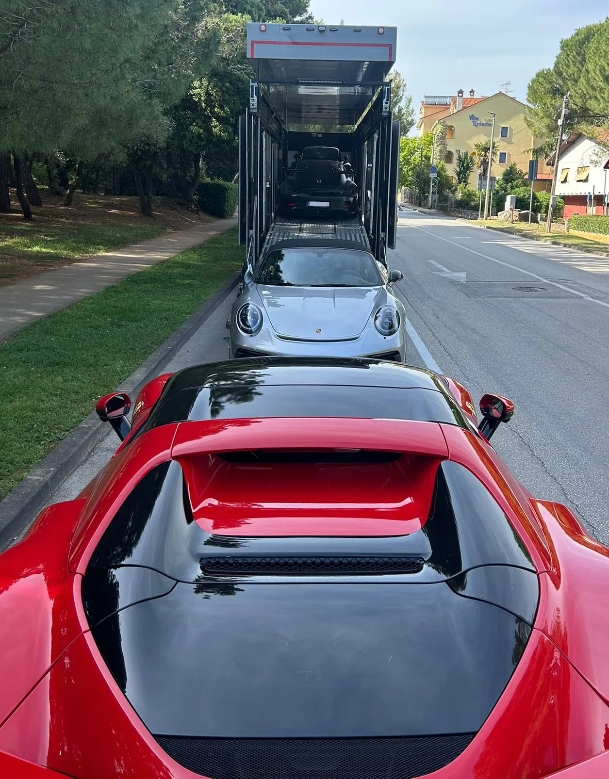 Rode Ferrari op een kustweg met een autotransporter erachter