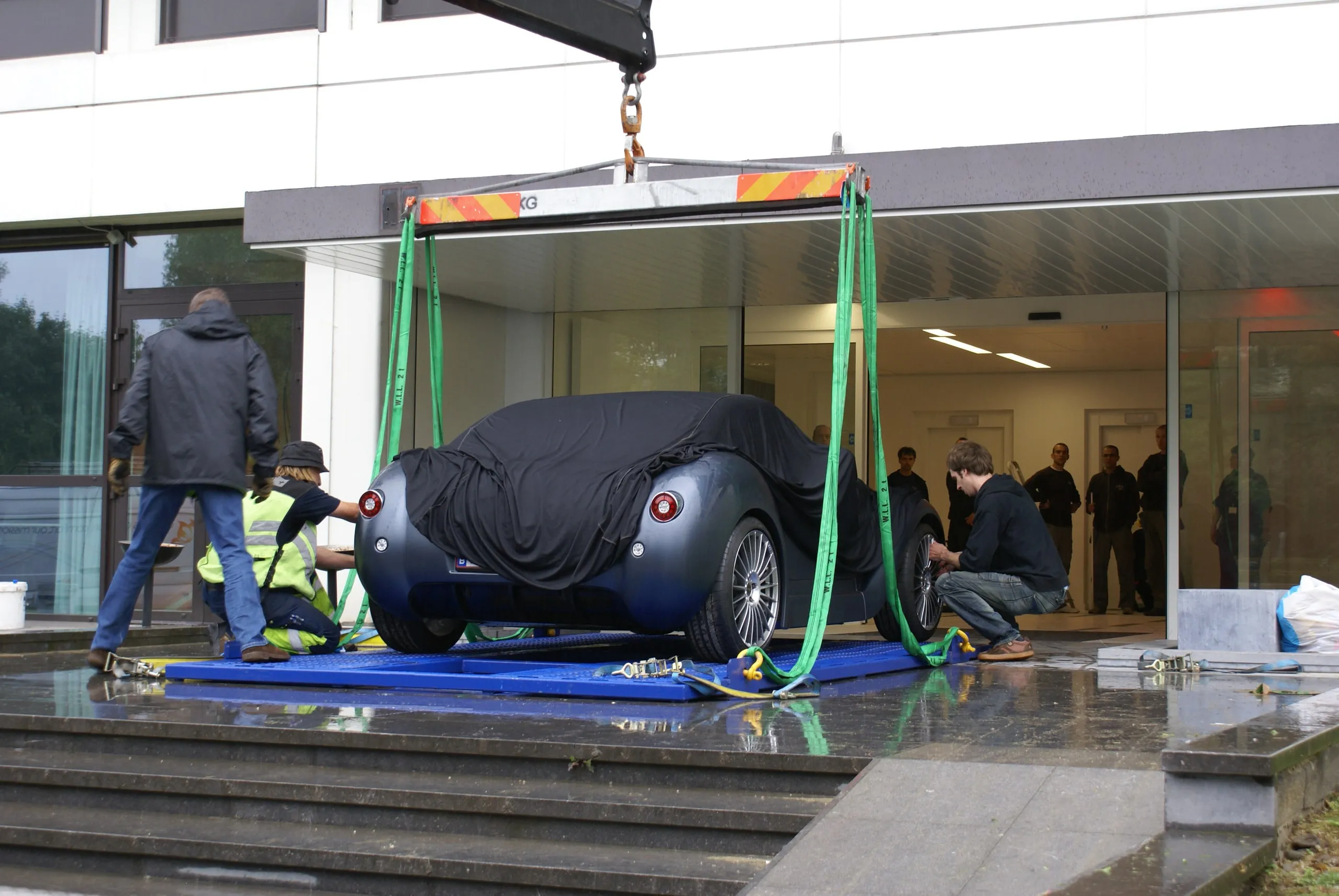 Afgedekte conceptcar met een kraan door de glazen gevel van een showroom getild