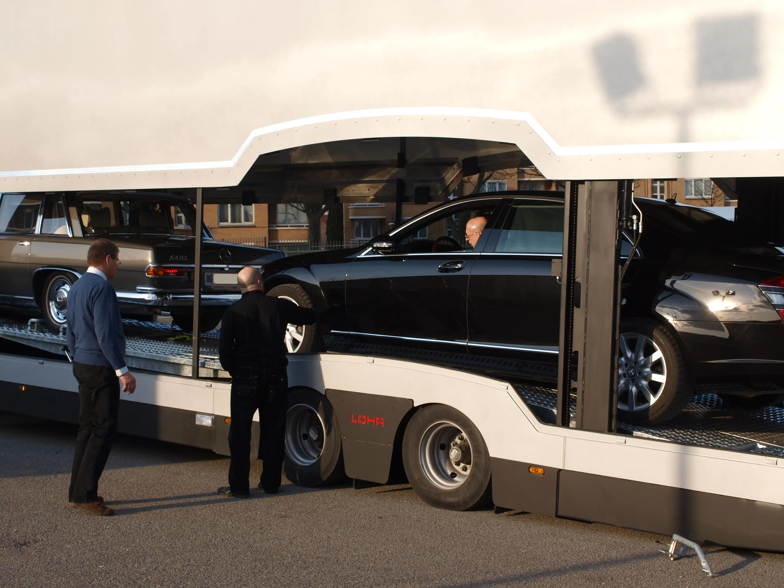 Twee mannen naast een geladen transporter met een donkere klassieke wagen op het dek