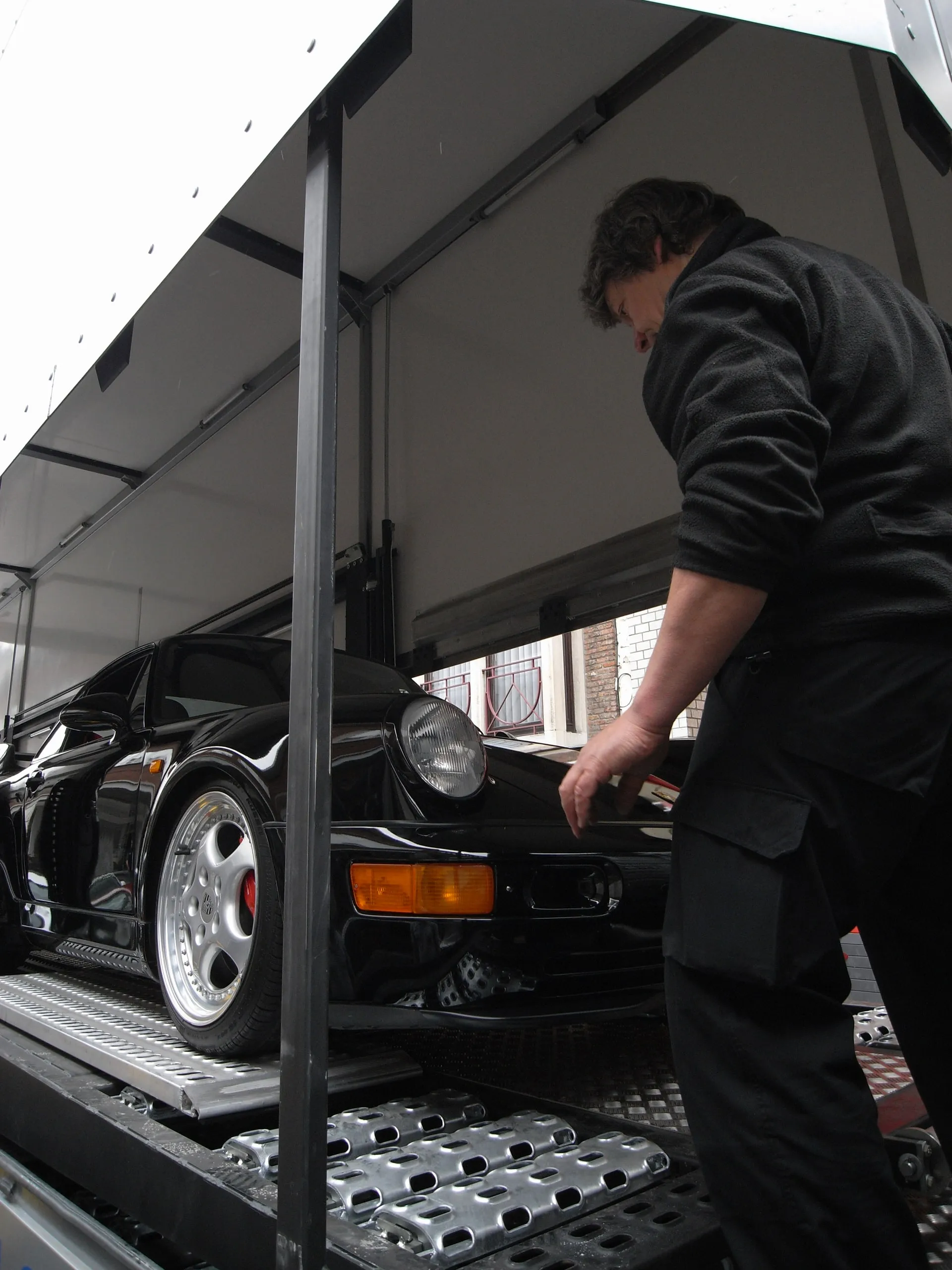 Crewlid naast een zwarte luchtgekoelde Porsche 911 Turbo in de transporter