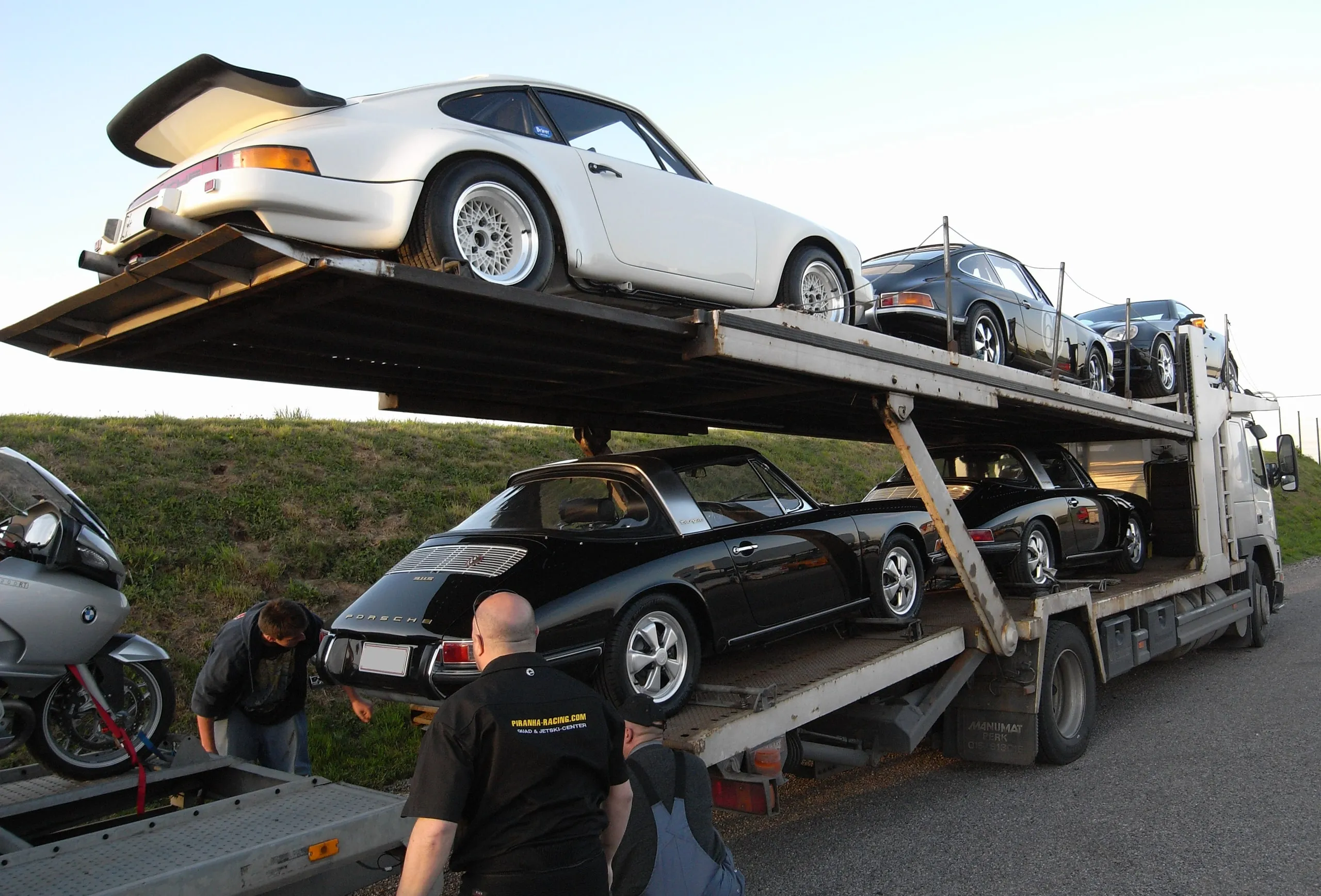 Deux équipiers chargeant des Porsche 911 sur les deux plateaux d'un camion