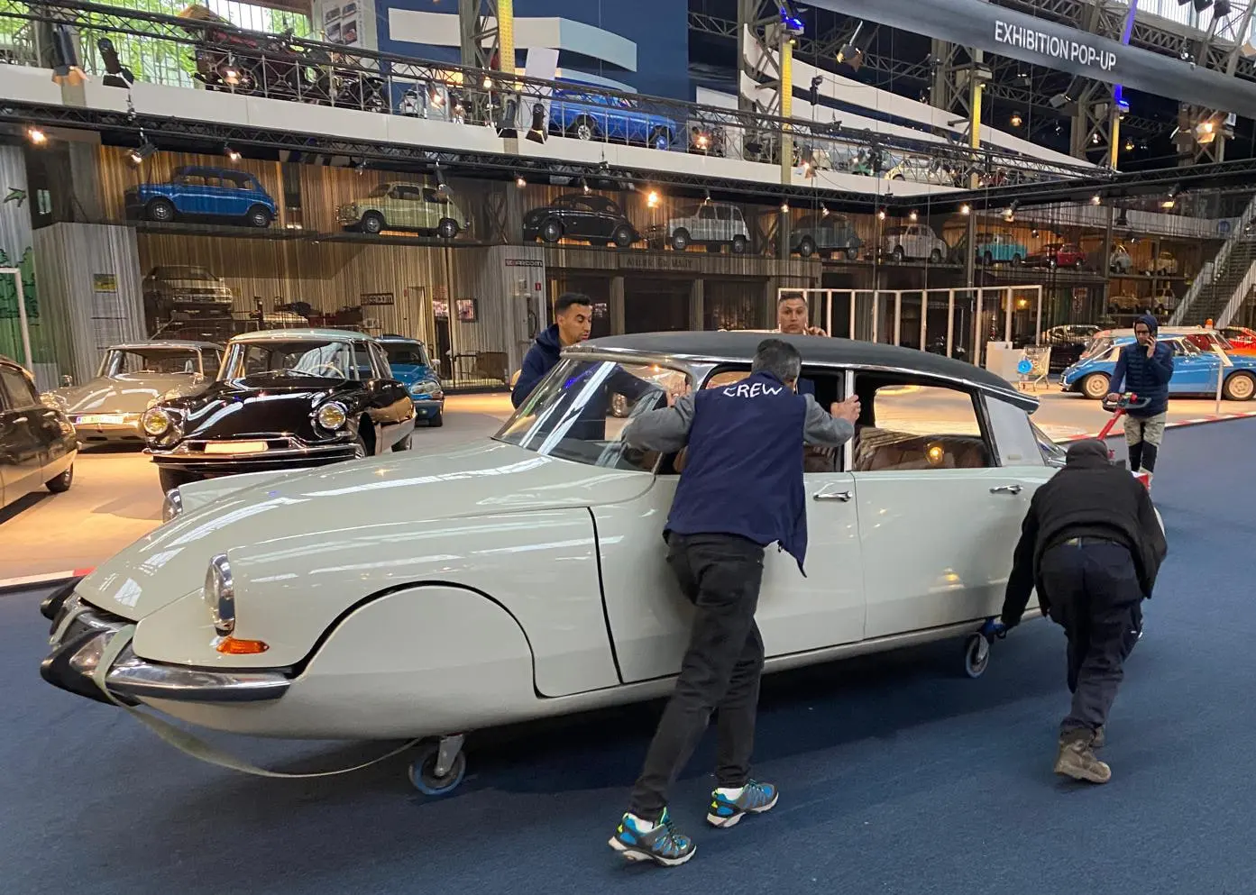 L'équipe pousse à la main une Citroën DS blanche dans la salle du musée