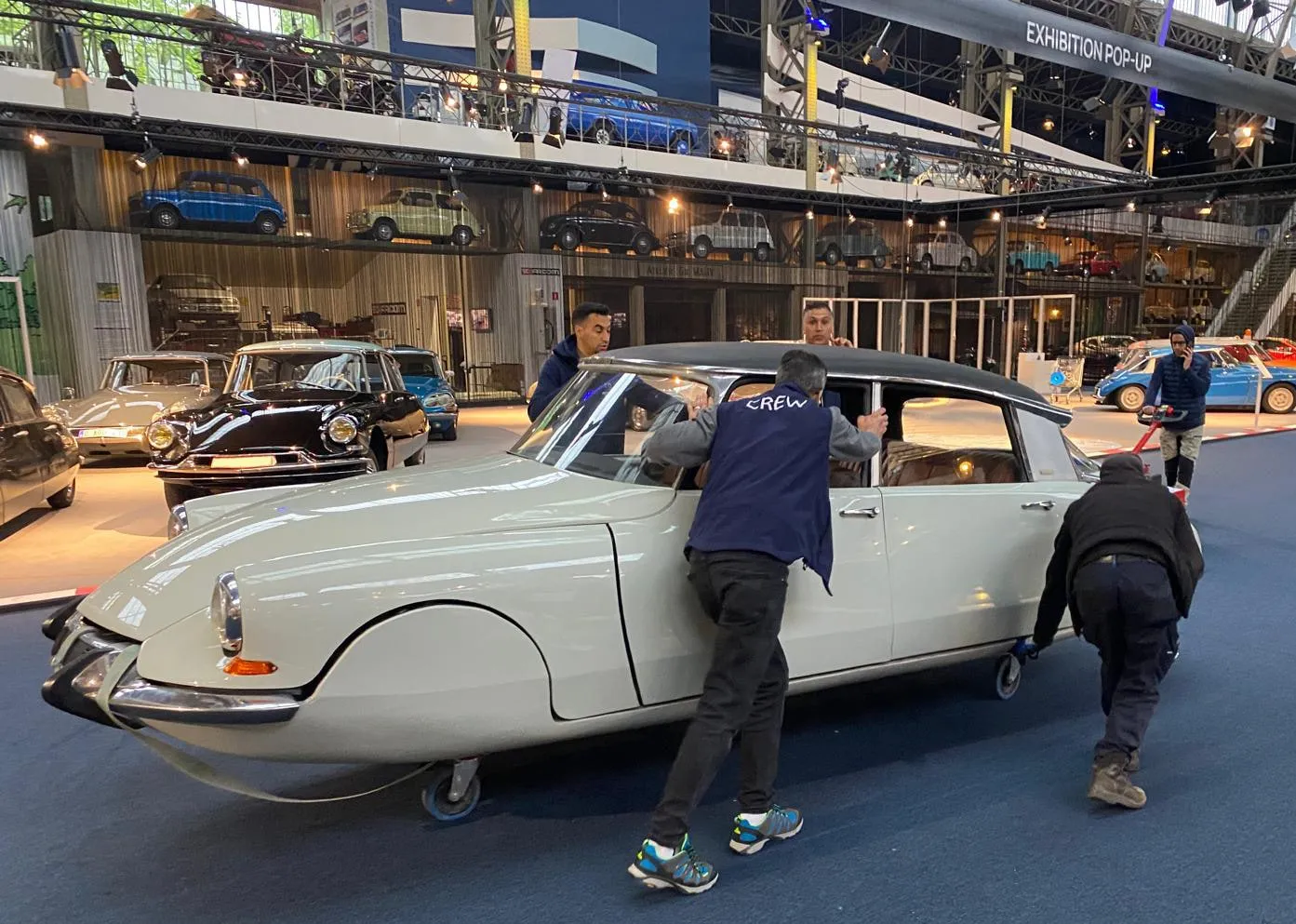 De ploeg duwt een witte Citroën DS met de hand over de museumvloer