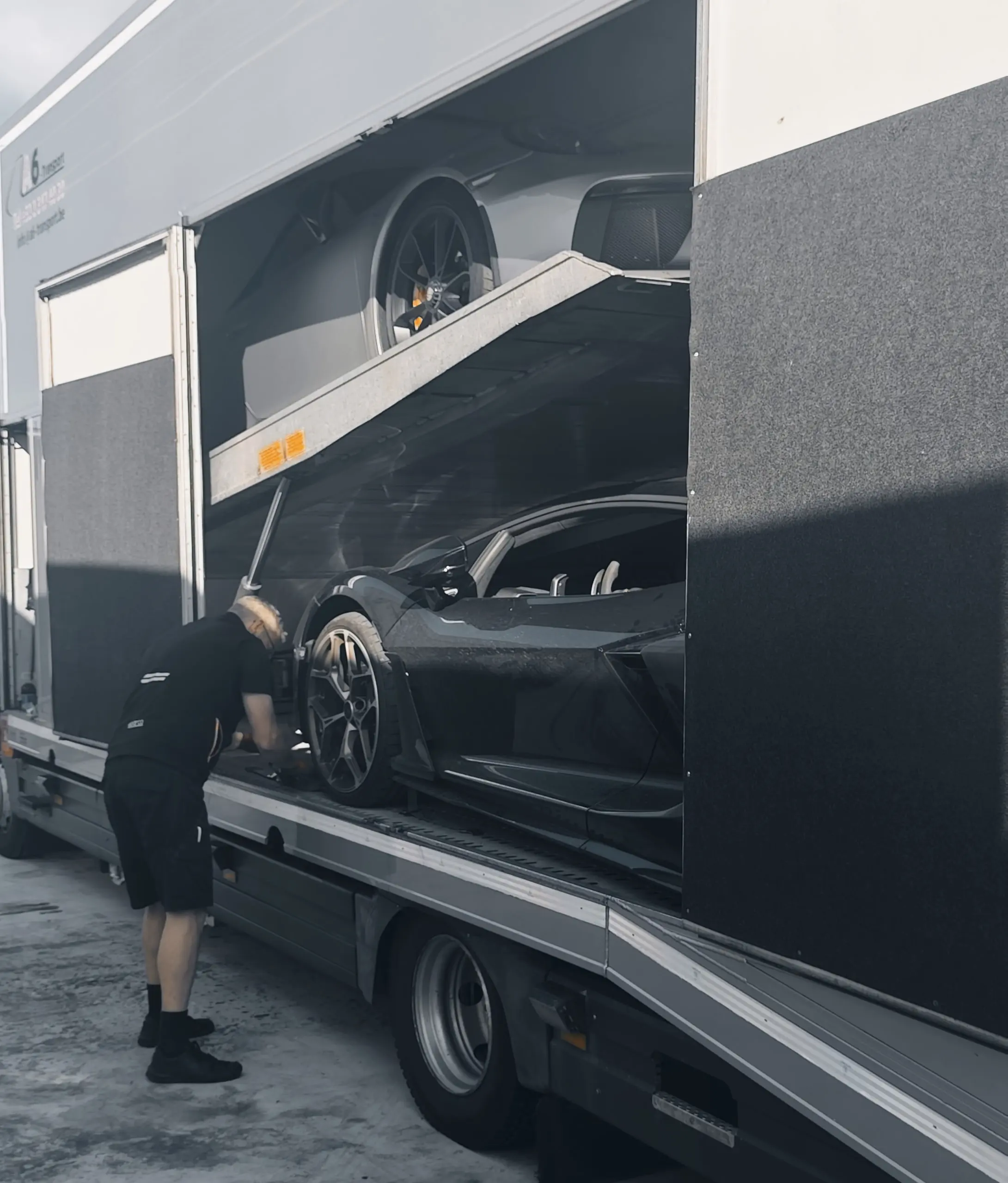 Crewmitglied zurrt einen Lamborghini im geschlossenen Transporter fest