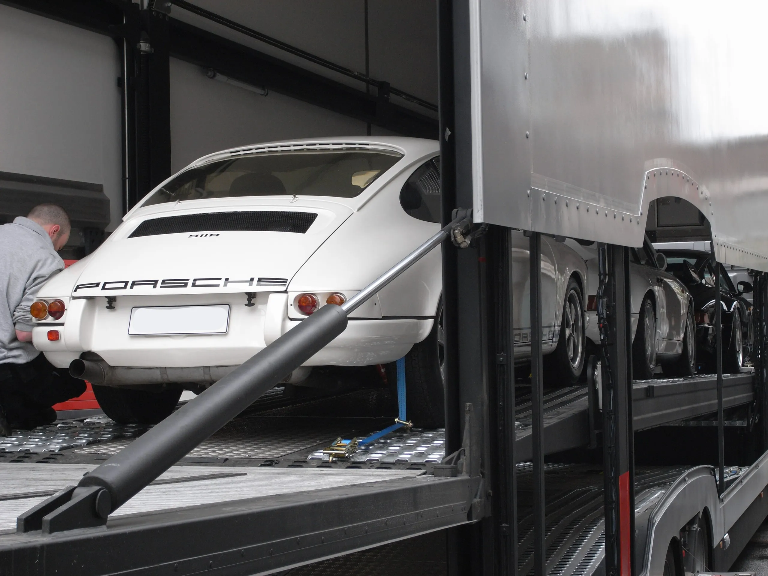 Achterzijde van een vroege witte Porsche 911 op het dek, een crewlid werkt vooraan
