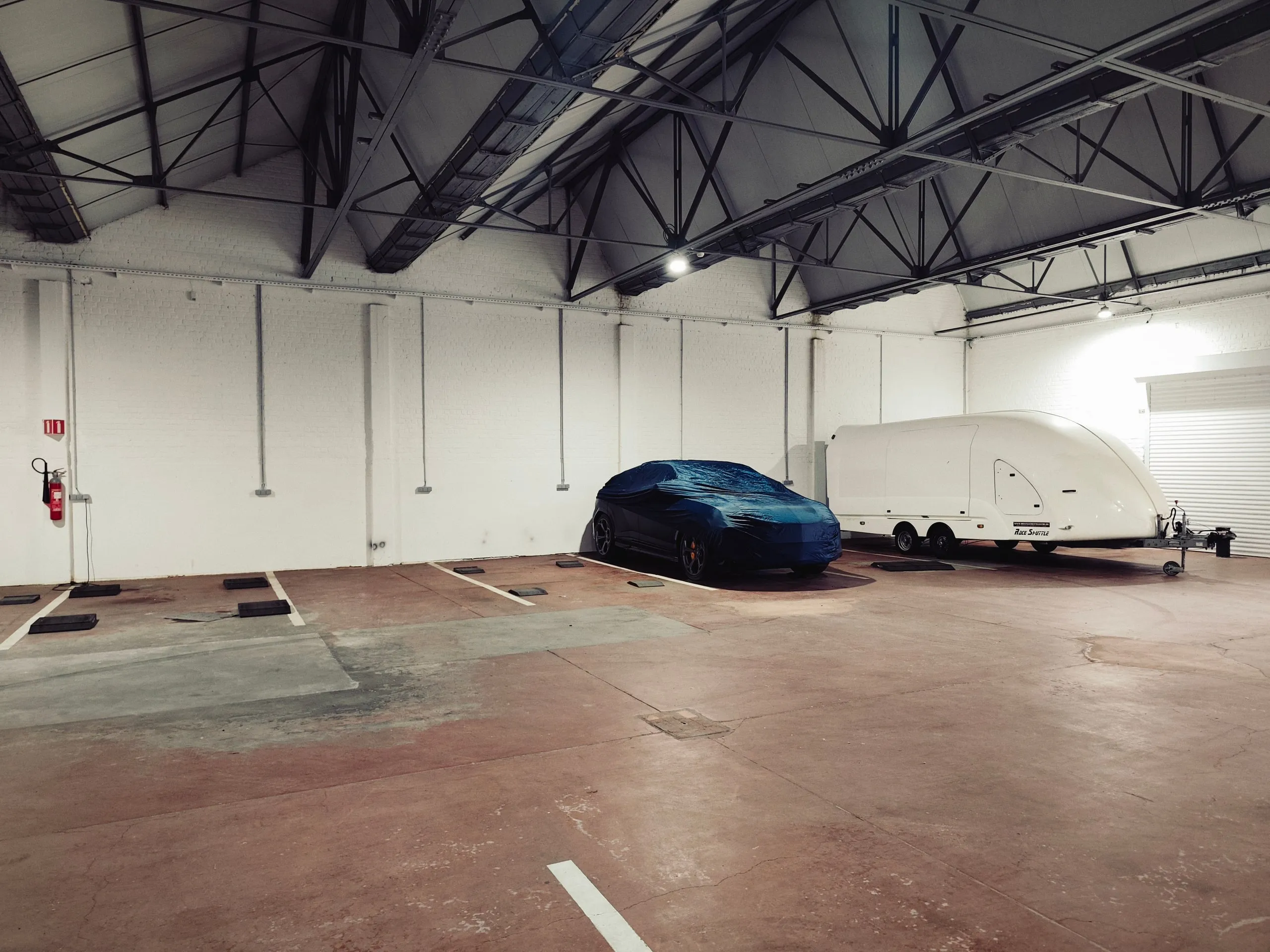 Plazas de guardacoches vacías, un coche cubierto y un remolque cerrado al fondo