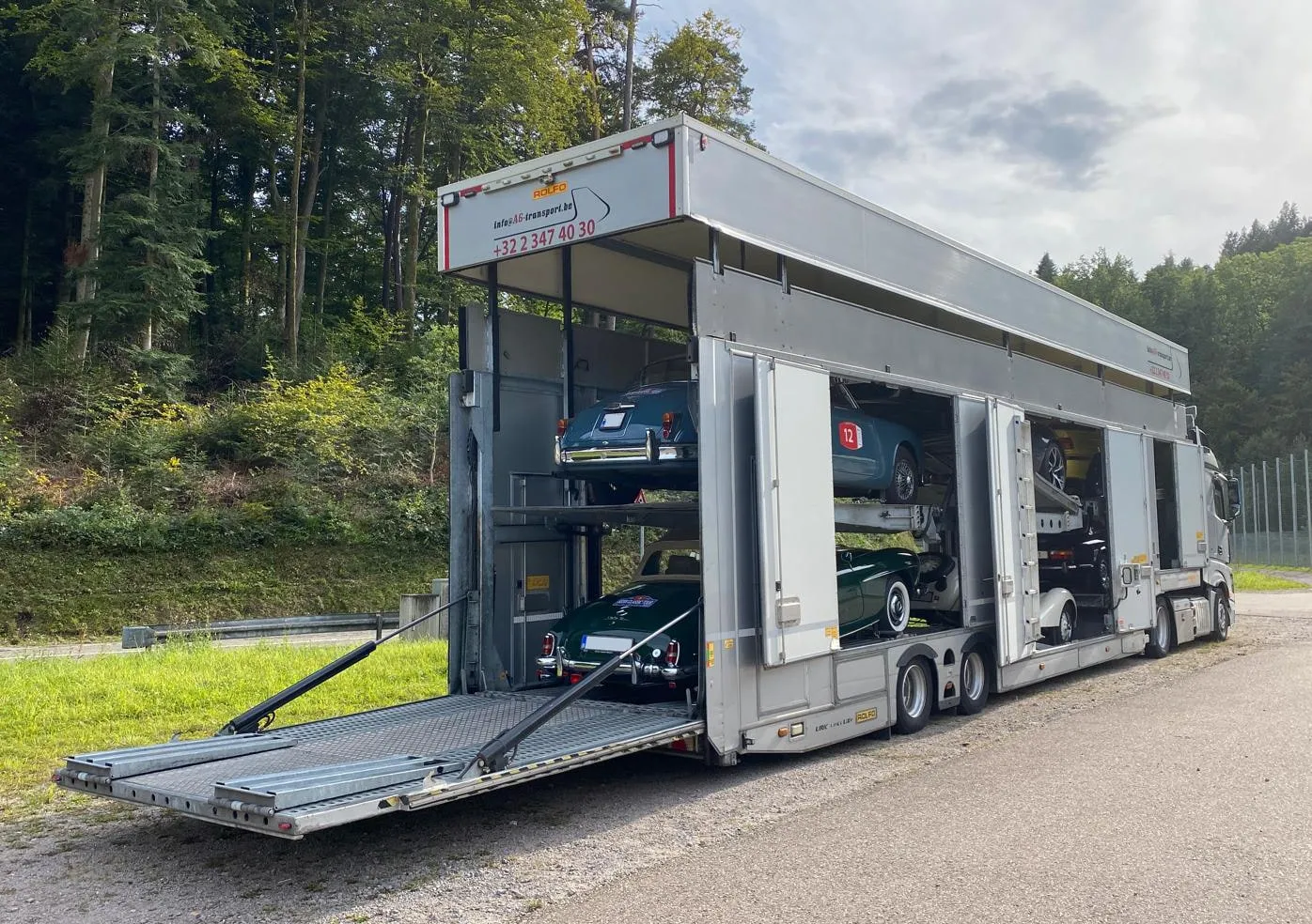 Gesloten transporter met kleppen neer en zijdeuren open op klassieke rallyauto's