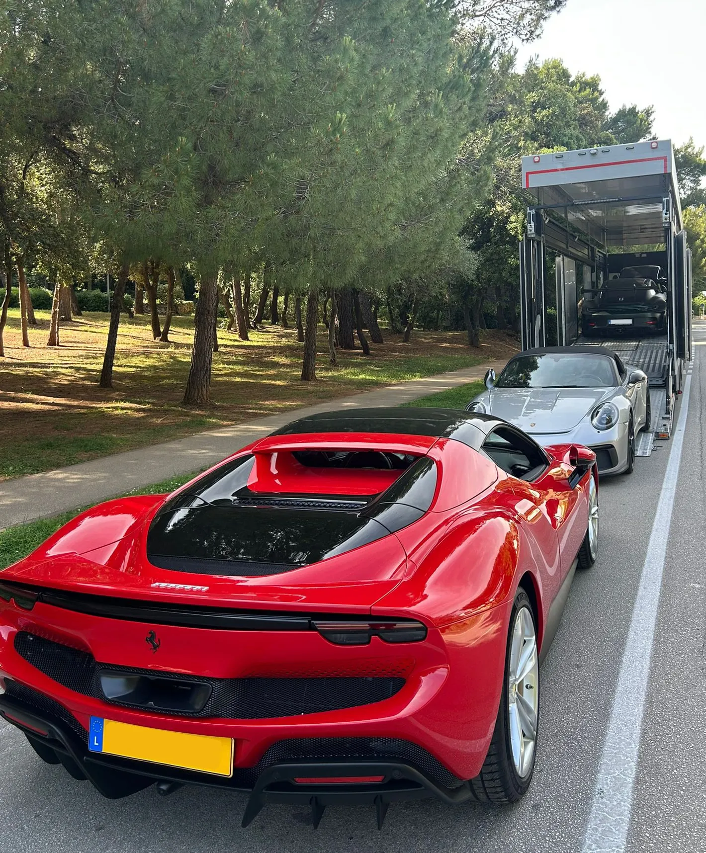 Rode Ferrari 296 GTS en Porsche 911 gelost langs een weg