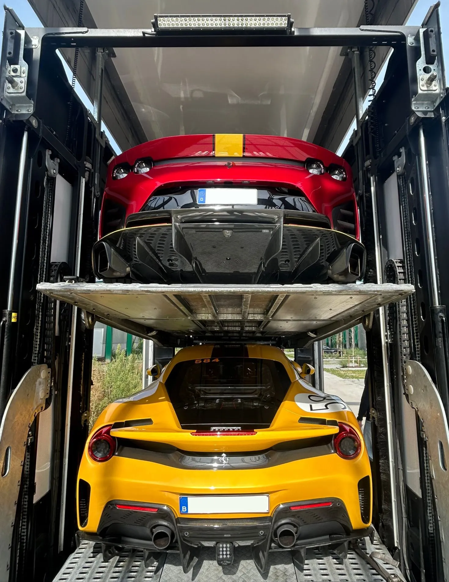 Rode Ferrari op het bovendek en gele Ferrari 488 Pista eronder, gezien door de open achterdeuren