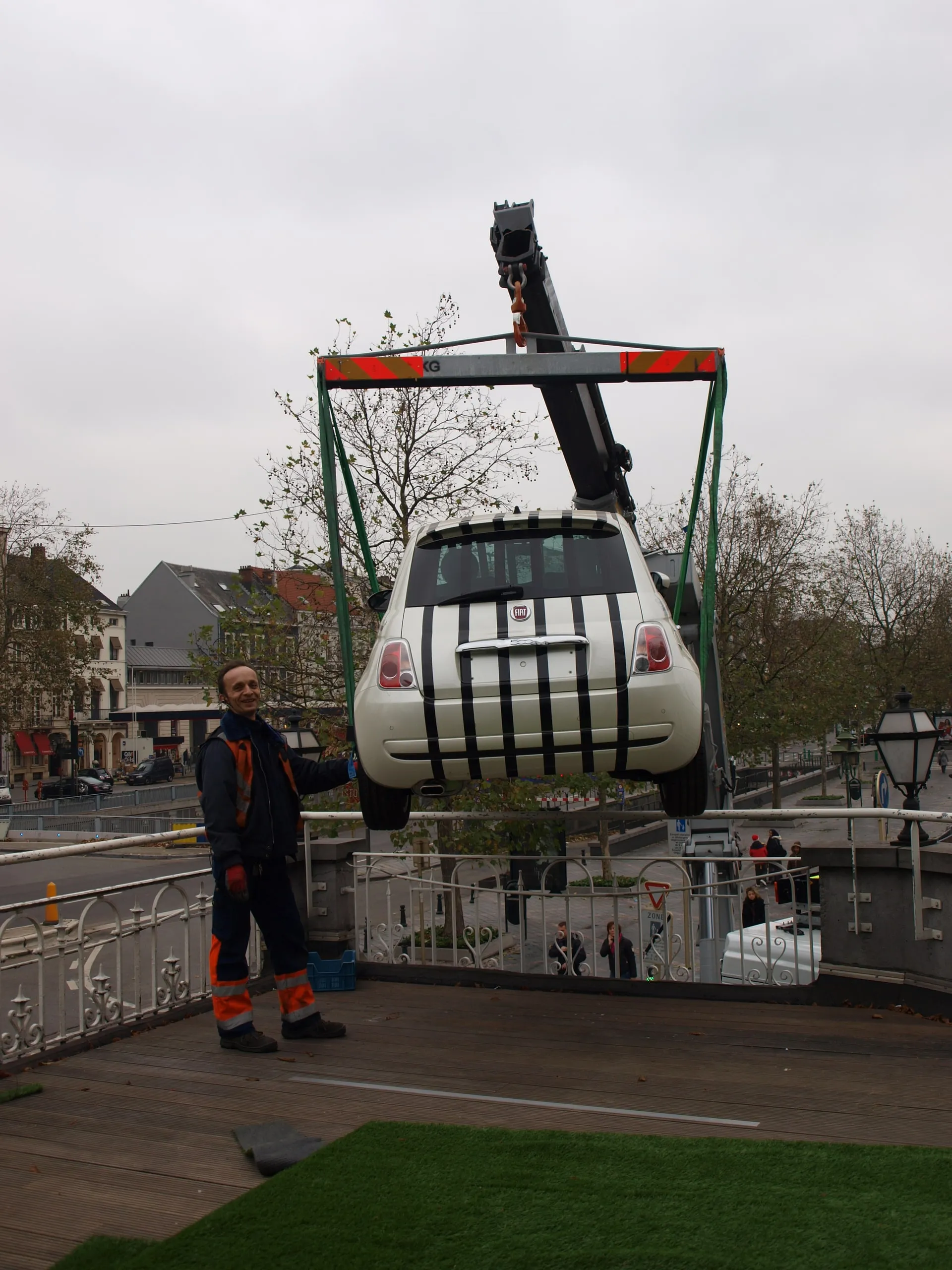 Fiat 500 in groene hijsbanden boven de straat, een crewlid eronder