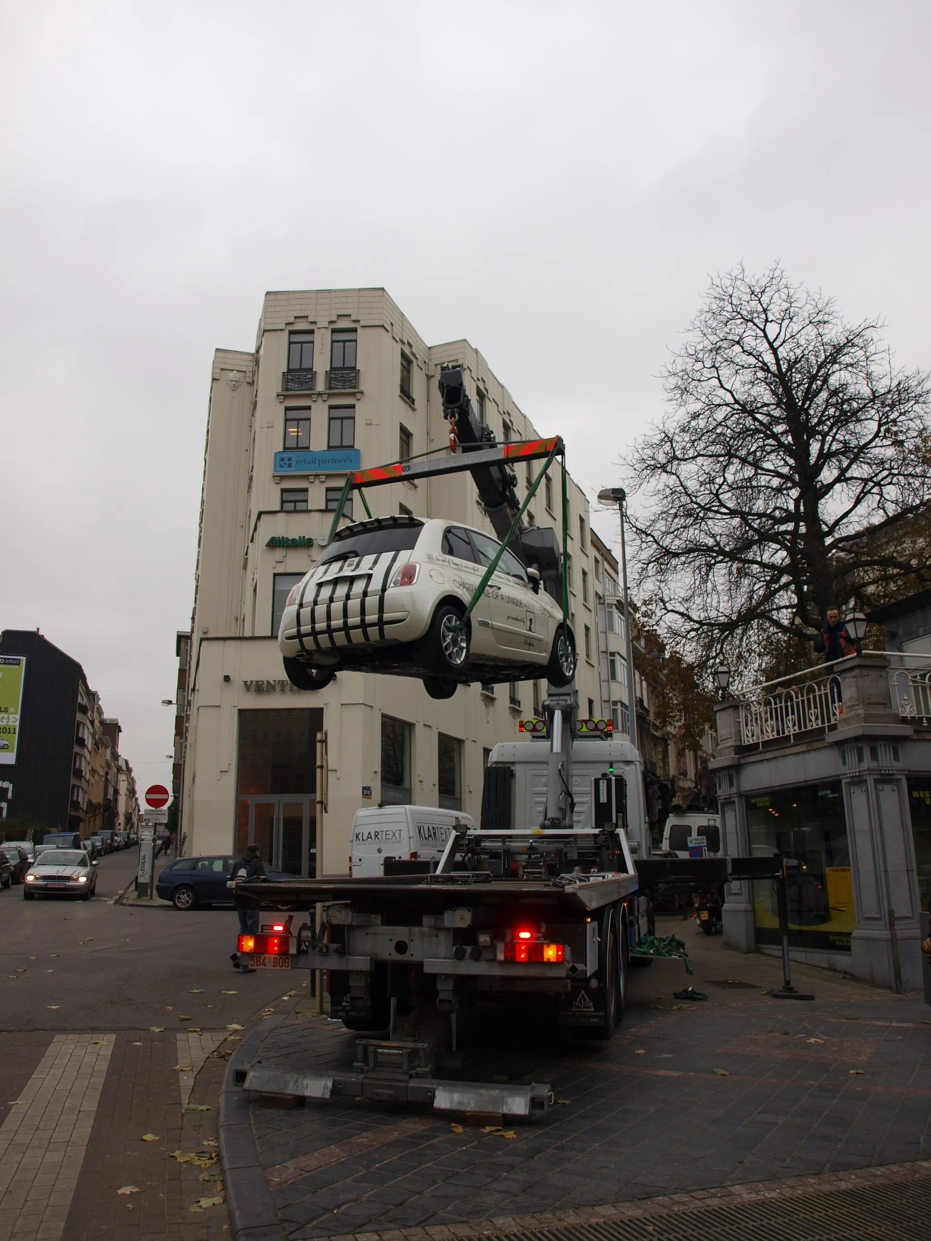 Fiat 500 door een kraanwagen boven een Brusselse laan getild