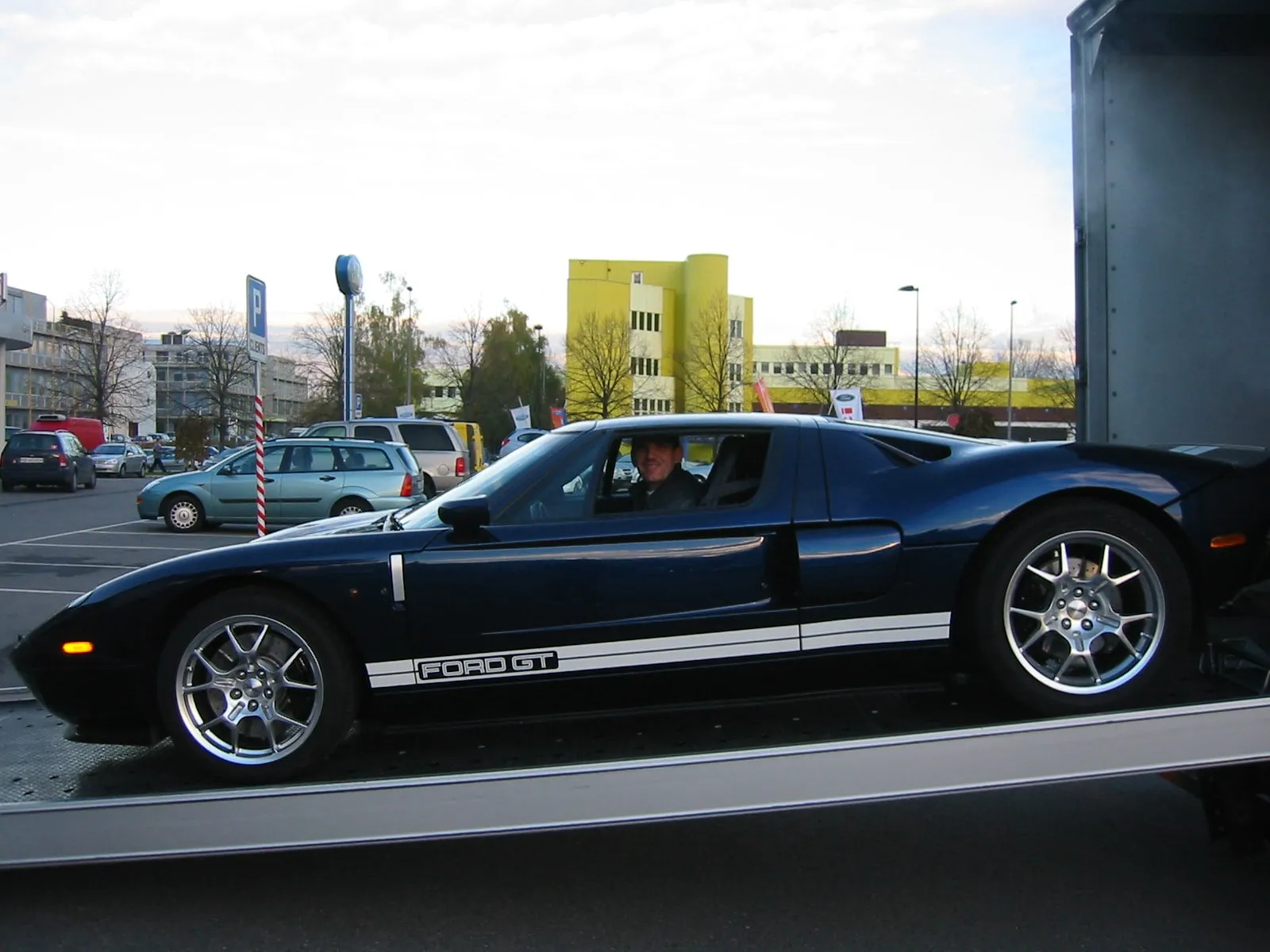 Blauwe Ford GT met witte strepen op het dek van een gesloten transporter