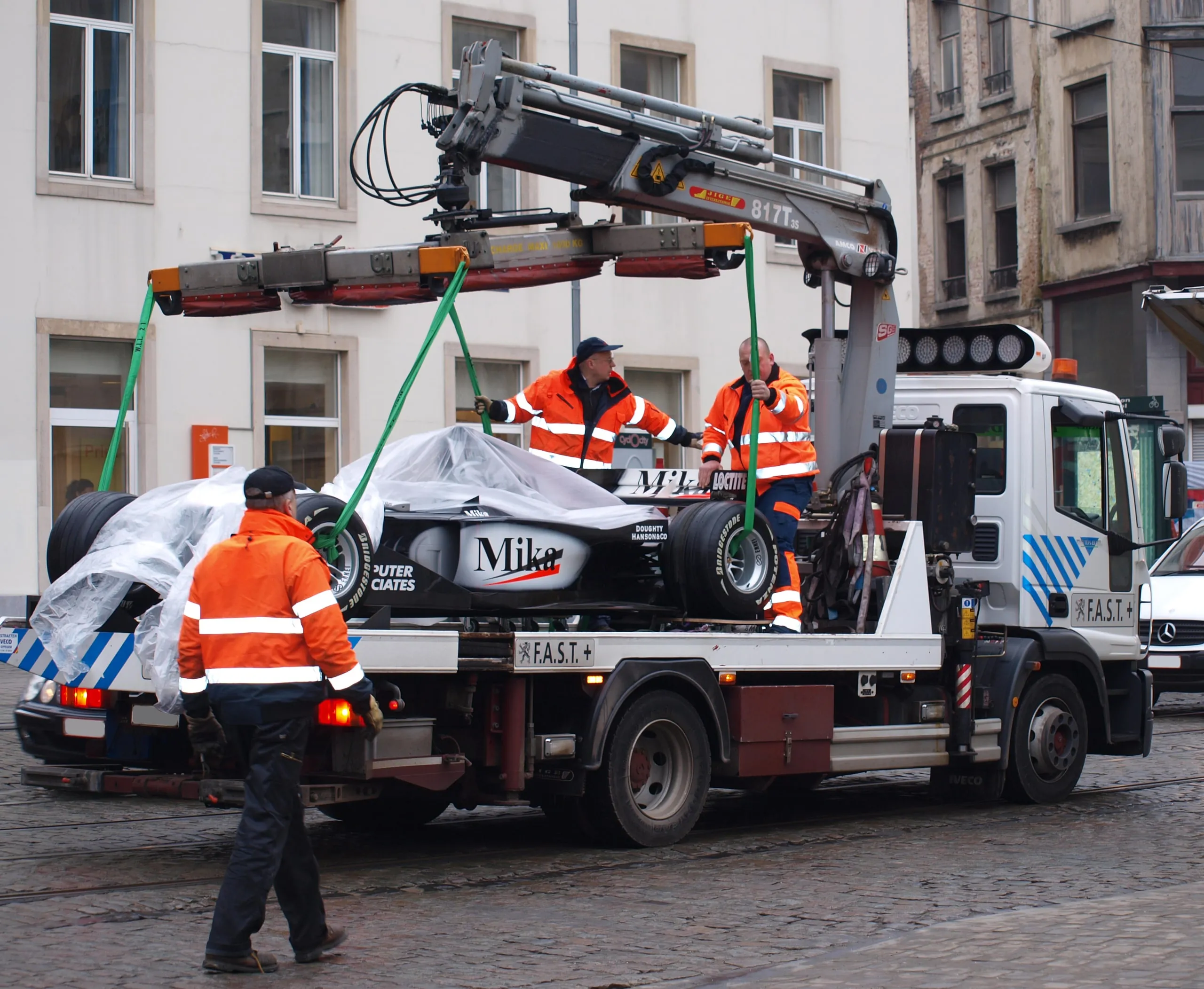 Formule 1-wagen door een kraanwagen opgetild in een Brusselse straat, de ploeg begeleidt hem