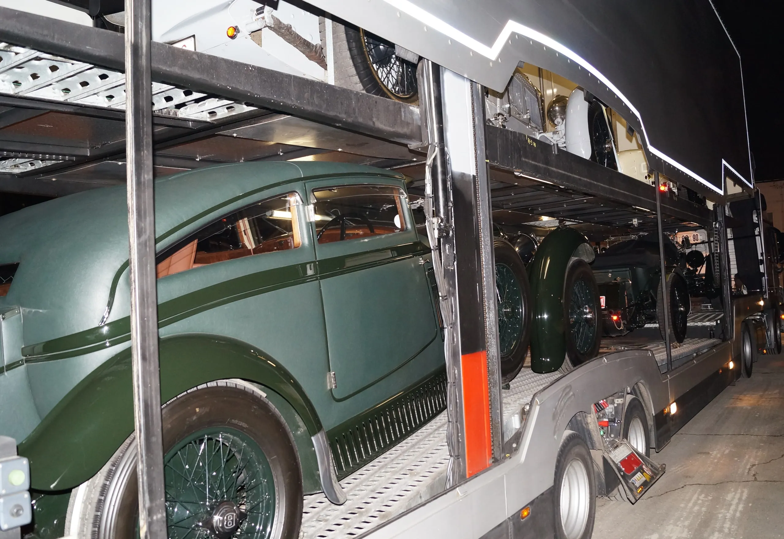 Donkergroene klassieke wagen met spaakwielen op het onderdek van een transporter