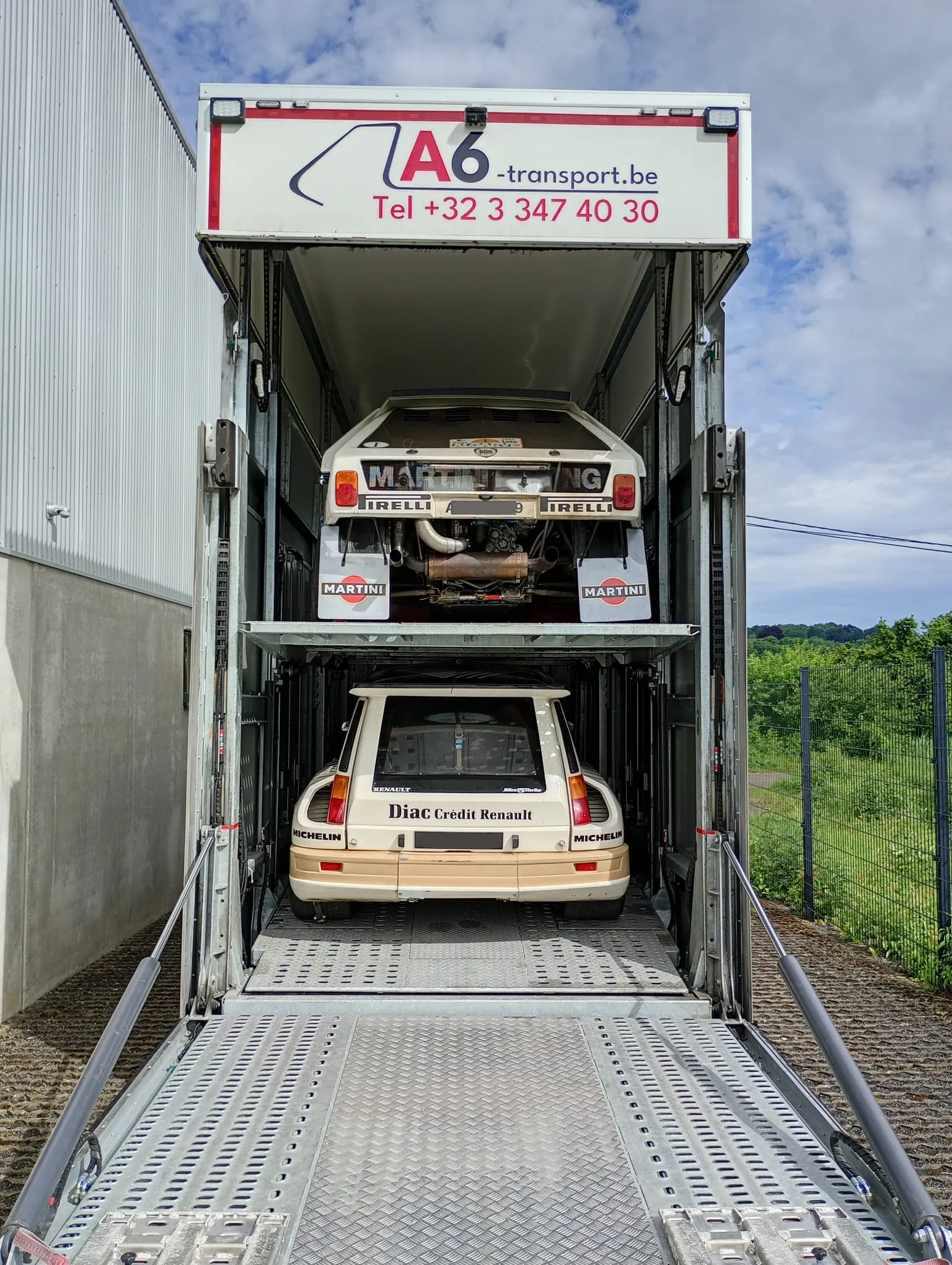 Groep B-rallywagens op beide dekken van een gesloten transporter