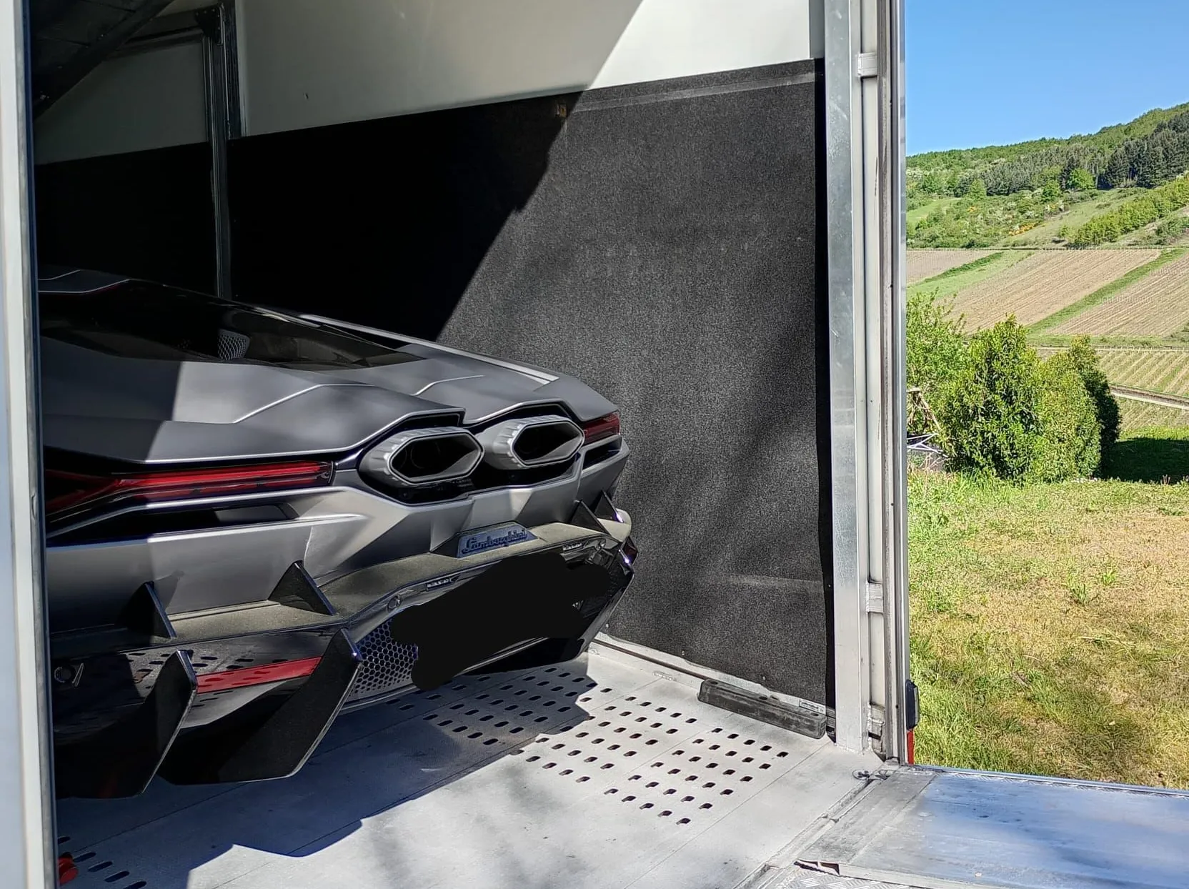 Achterzijde van een Lamborghini Revuelto in een transporter, wijngaard erachter