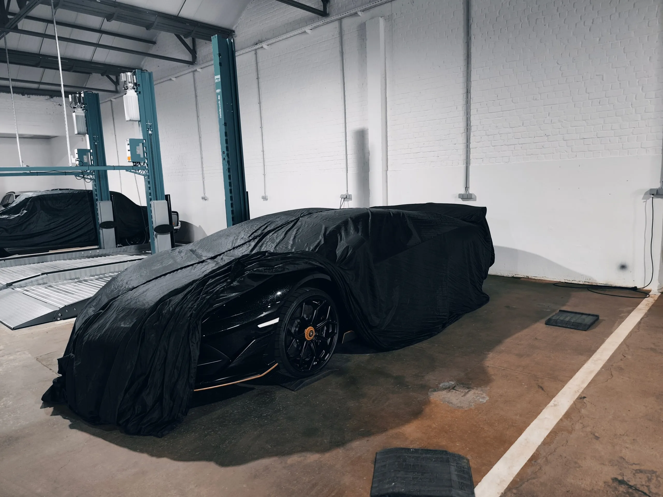 Lamborghini totalmente cubierto con una funda negra en su plaza, otros coches cubiertos detrás