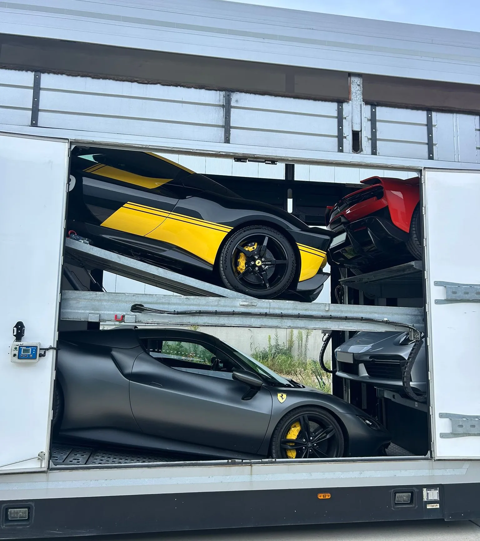 Zwarte Ferrari met gele baan op het bovendek, matzwarte Ferrari eronder, zijdeuren open