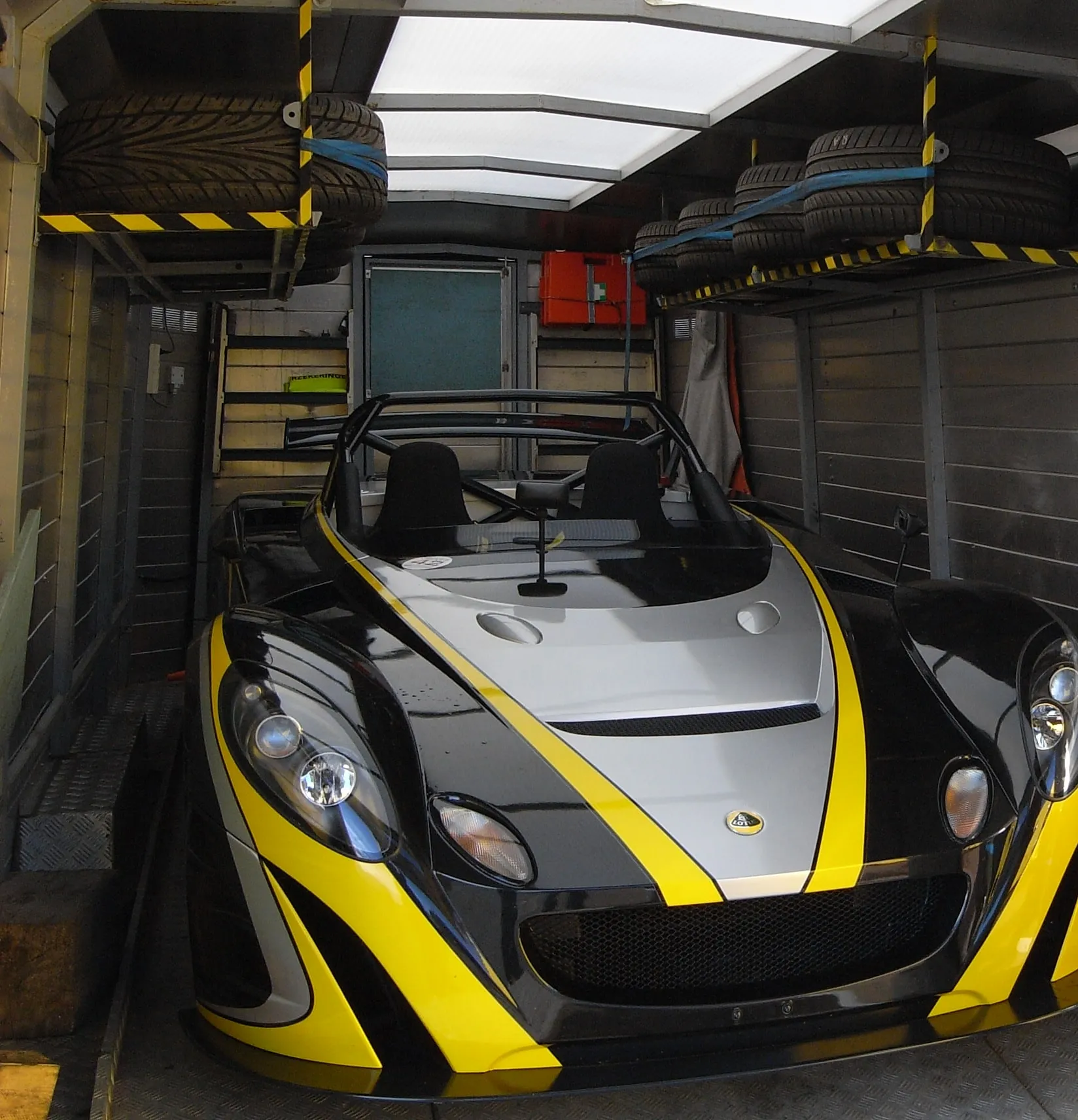 Geel-zwarte Lotus-circuitwagen in een racetransporter, reservebanden erboven