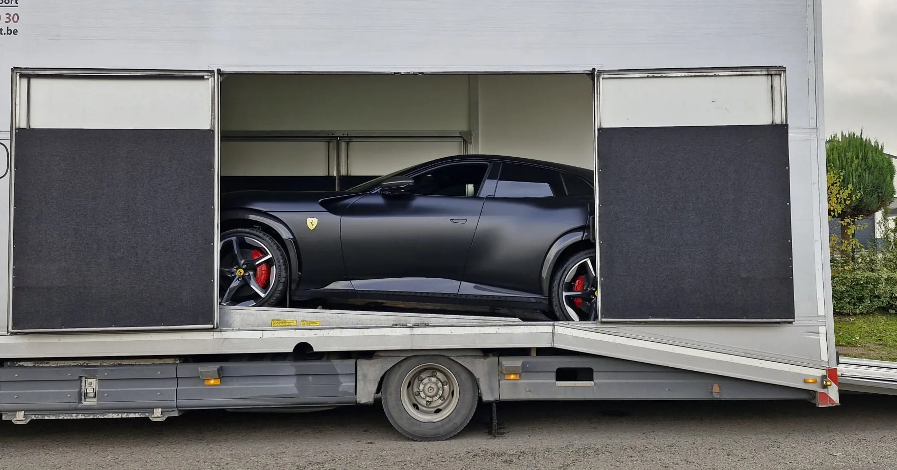Matzwarte Ferrari Purosangue in de gesloten transporter, zijdeuren open