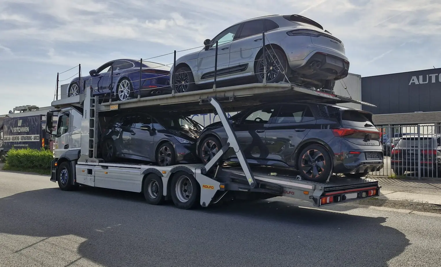 Camion ouvert à deux niveaux chargé de quatre voitures modernes devant un garage