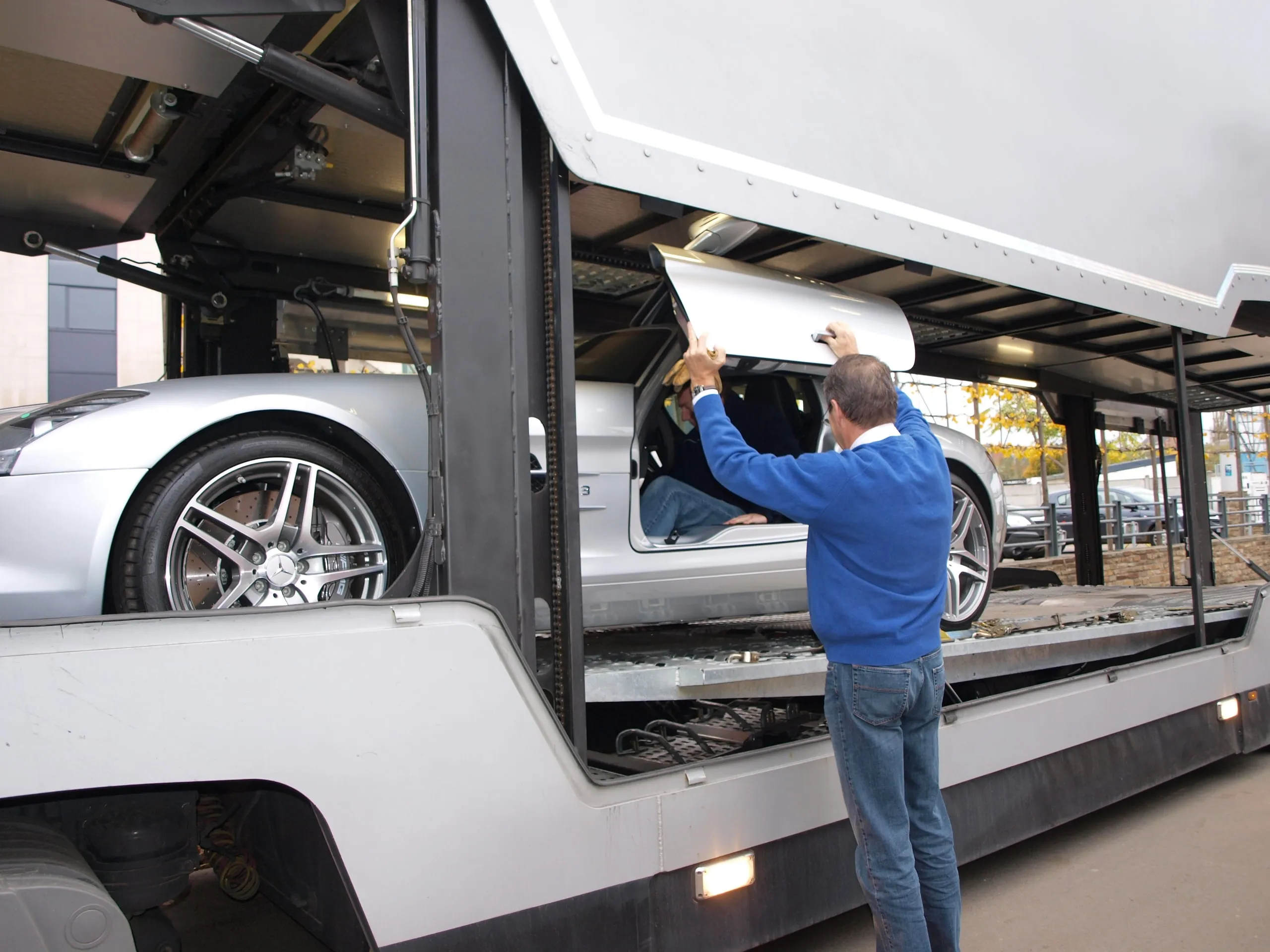Man fotografeert een witte Mercedes SLS AMG op de transporter voor het lossen