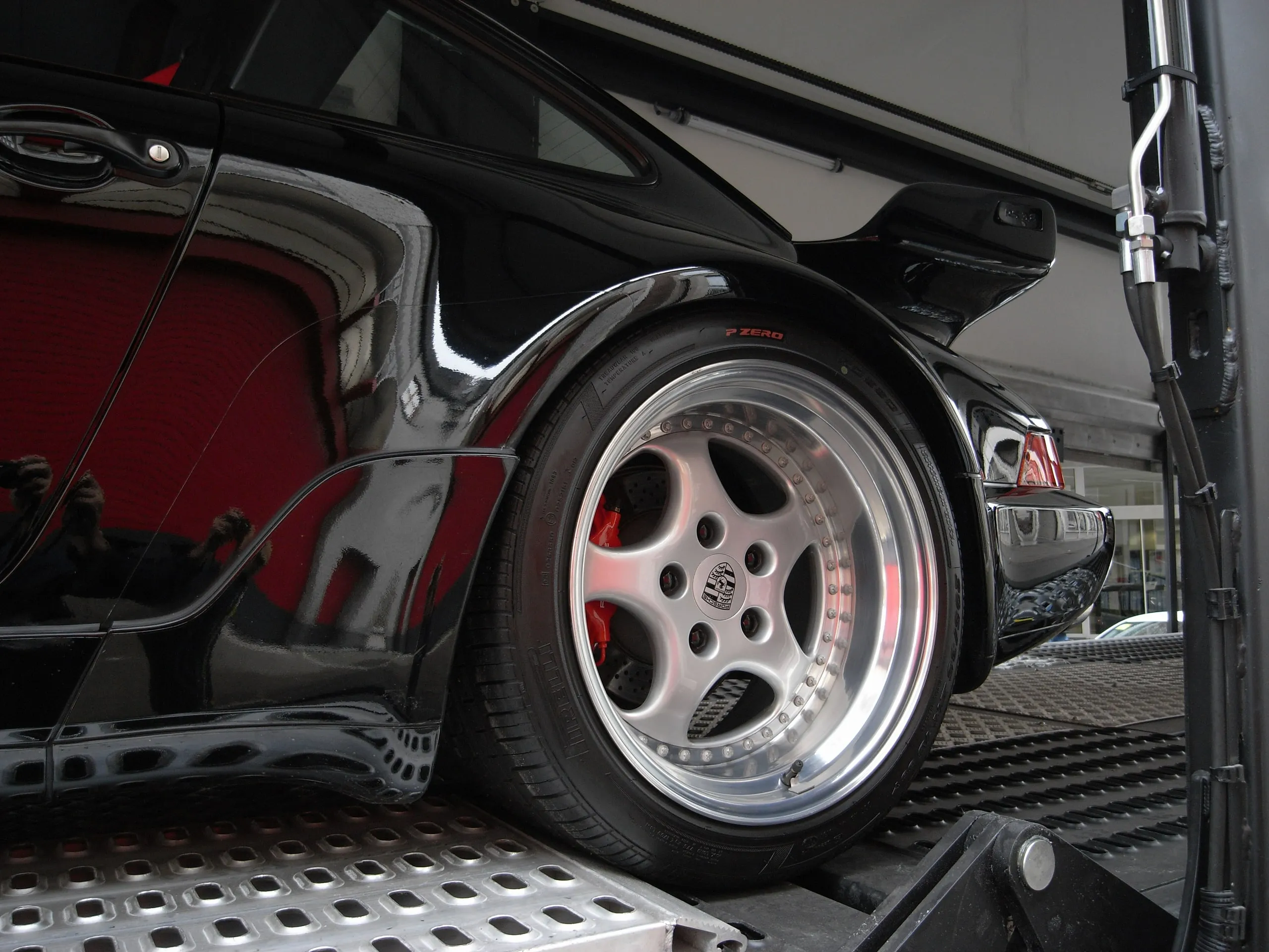 Velg met gepolijste rand van een zwarte Porsche 911 Turbo op een geperforeerd dek