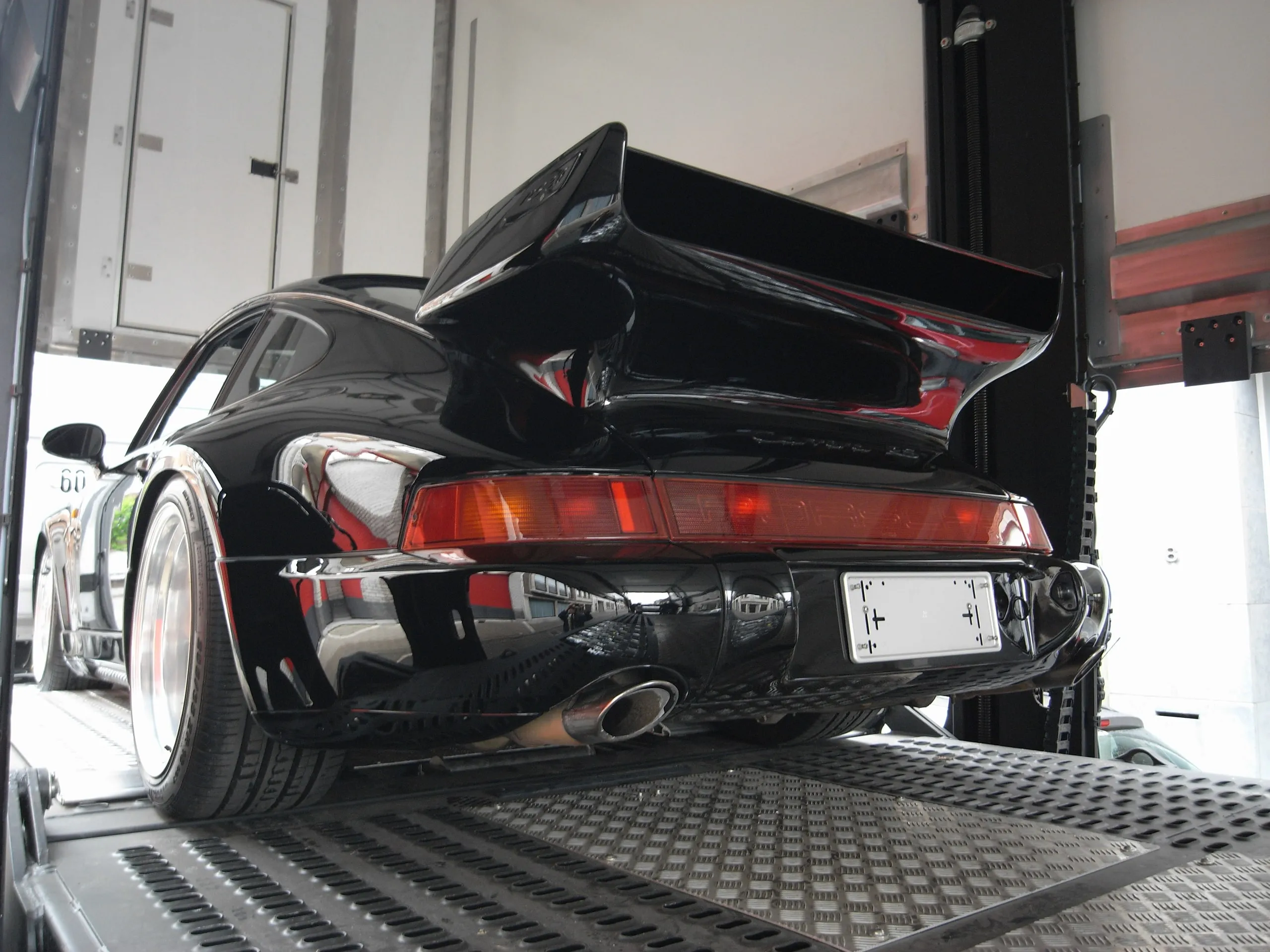 Achtervleugel van een zwarte Porsche 911 Turbo op het onderdek van een transporter