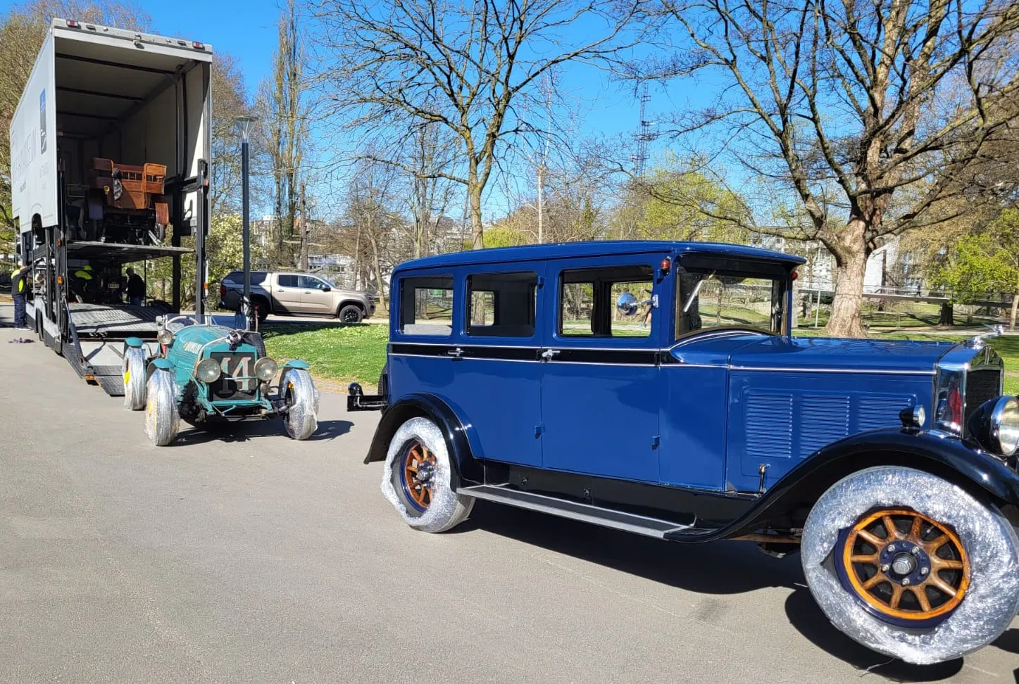 Berline bleue et voiture de course d'avant-guerre déchargées dans un parc