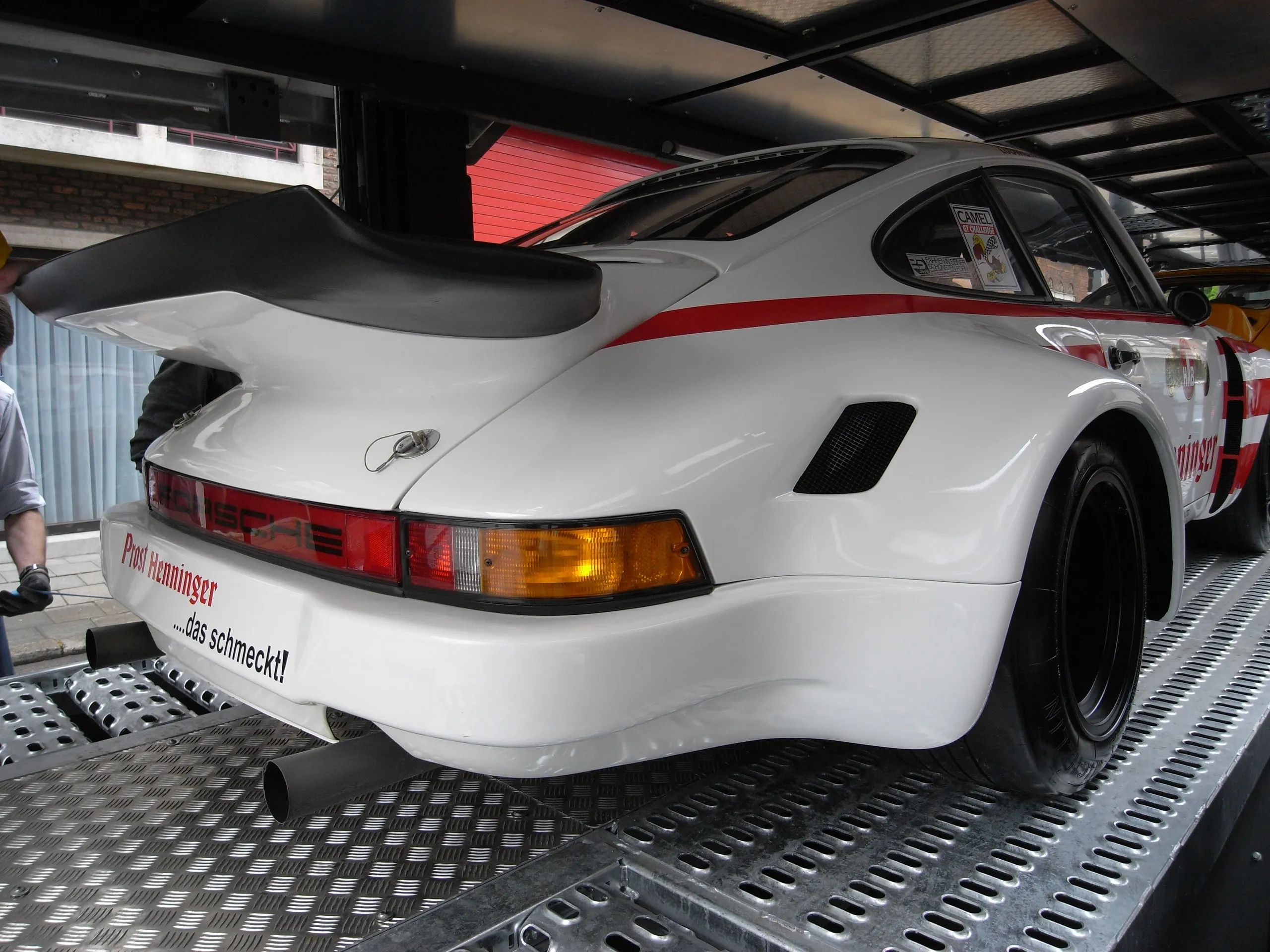 Witte Porsche 911-racewagen met grote achtervleugel op de plaat van de transporter