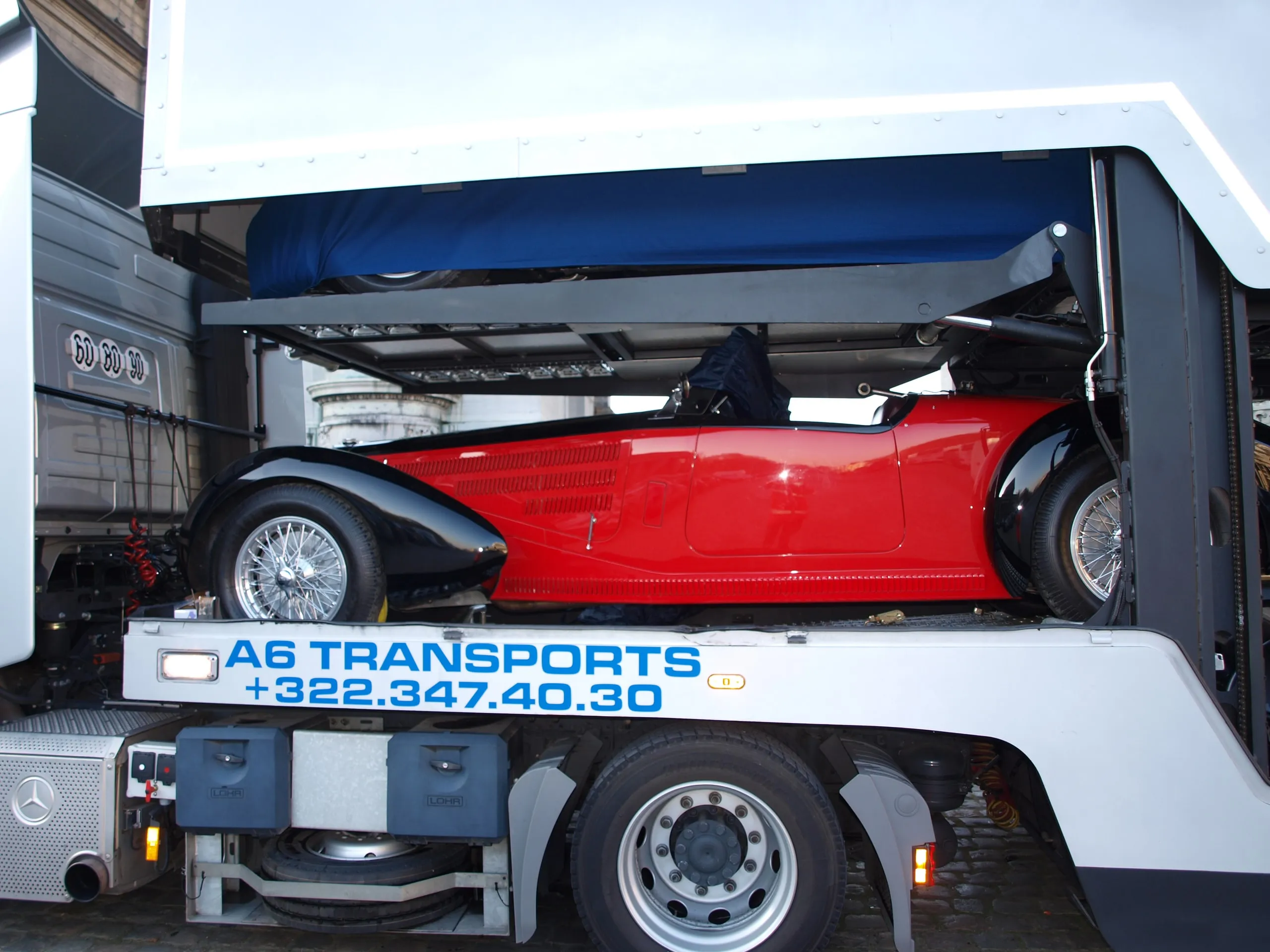 Rode vooroorlogse Bugatti-roadster op het bovendek van een transporter, platen neer