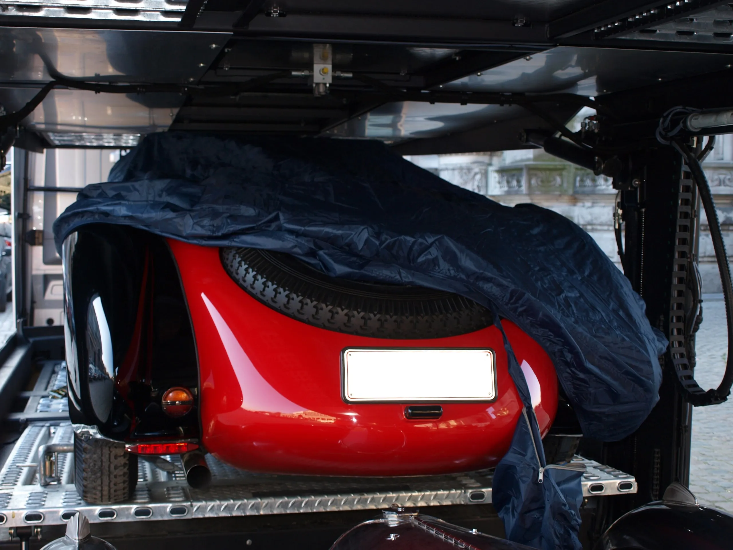 Rode vooroorlogse Bugatti-roadster half bedekt met een donker dekzeil op de transporter