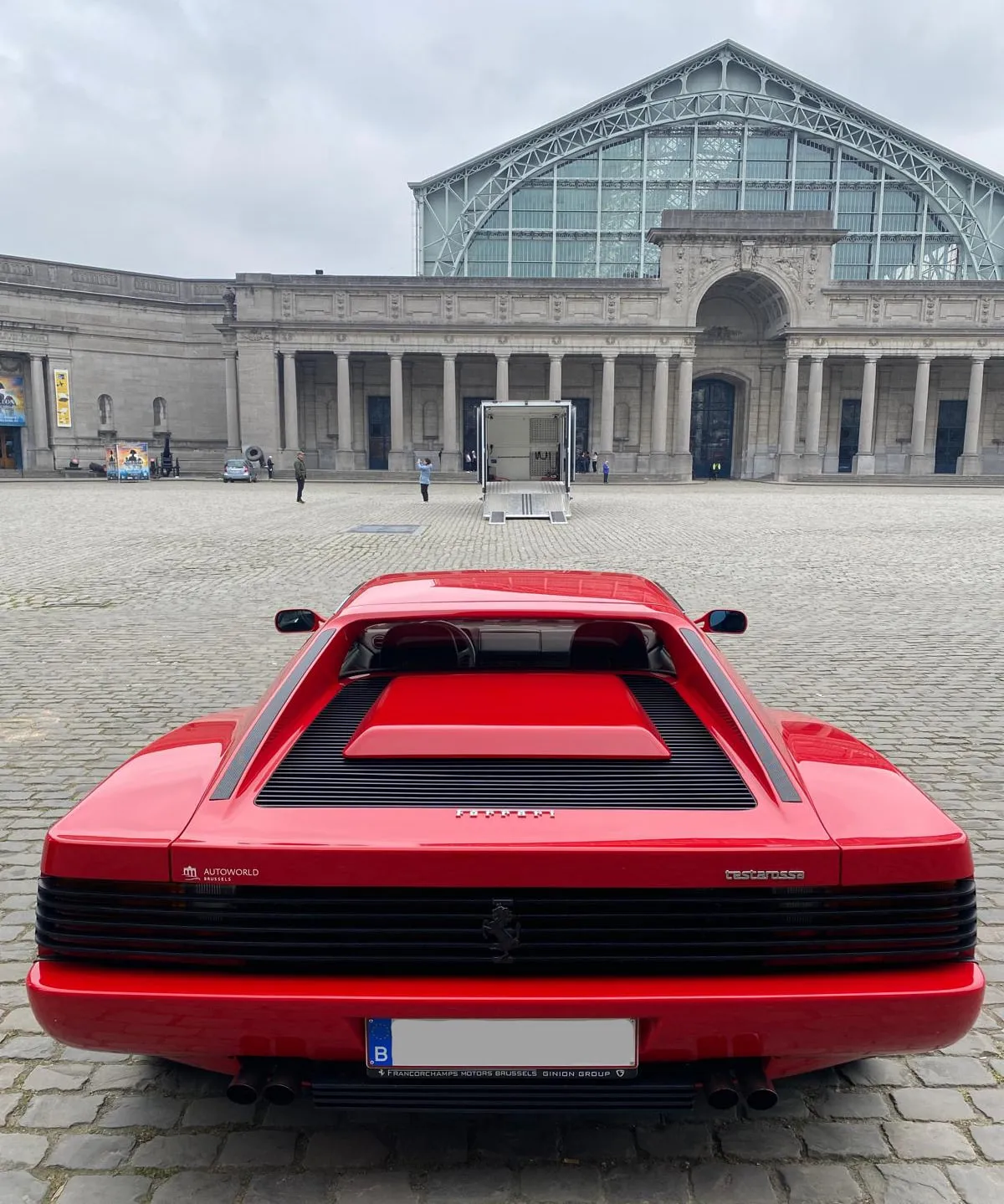 Rode Ferrari Testarossa op de kasseien van het Jubelpark, gesloten truck voor de museumingang