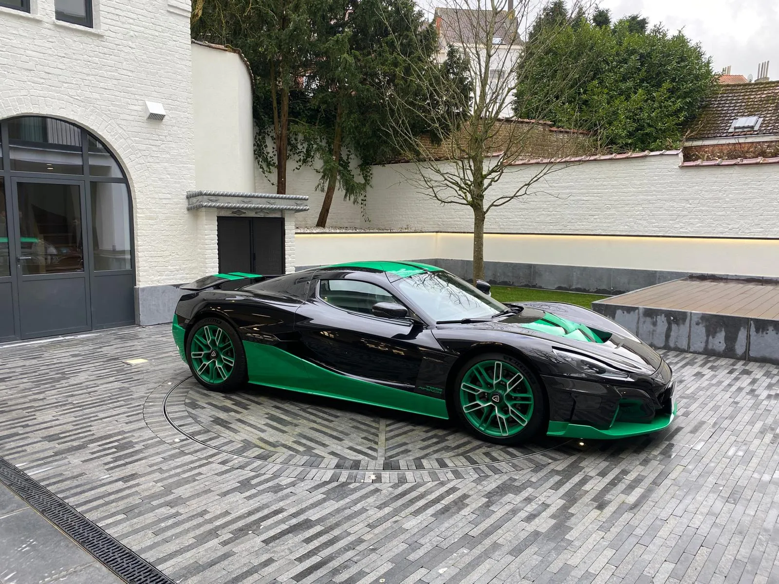Zwart-groene Rimac Nevera op een draaischijf in een private binnenkoer