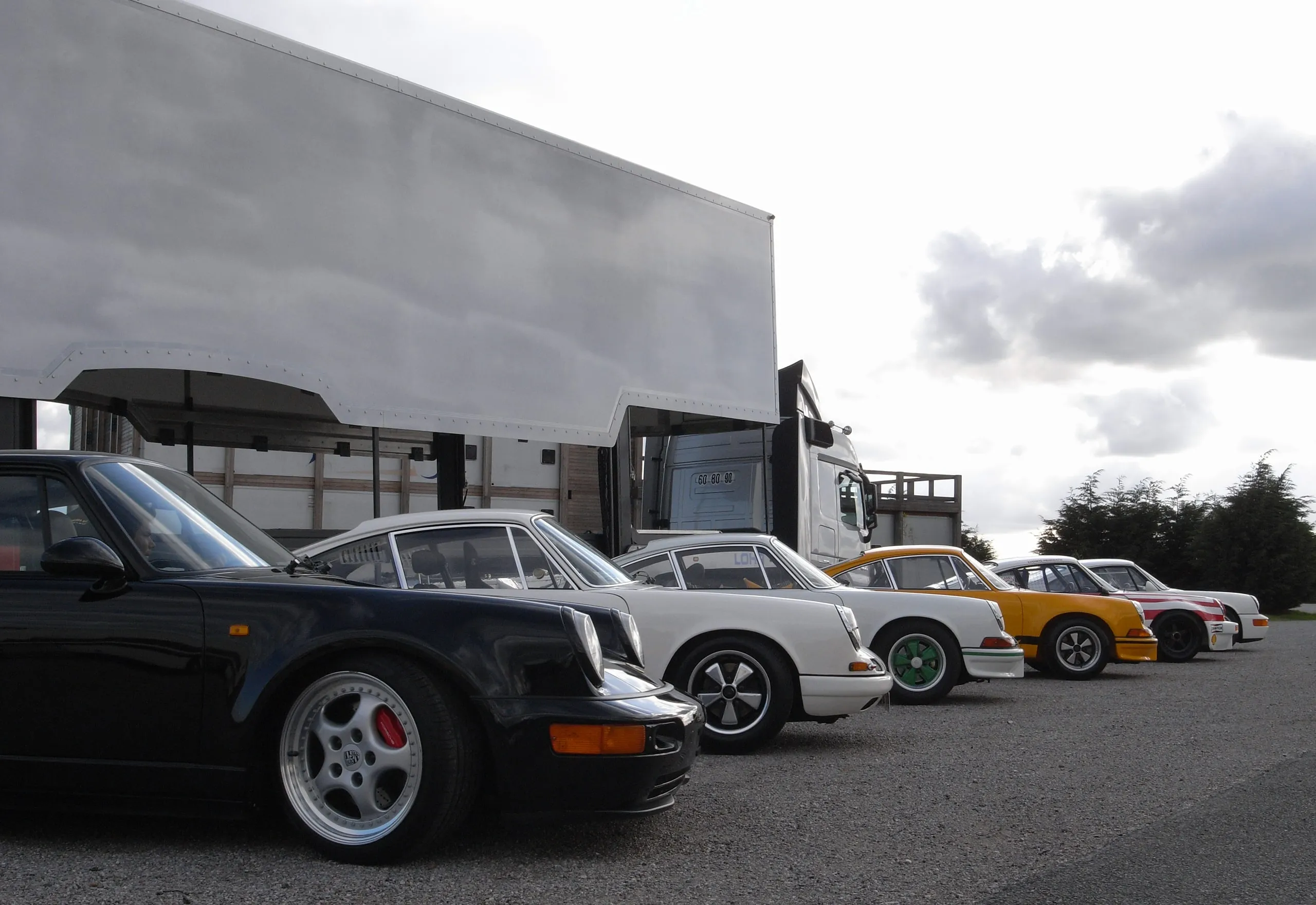 Rangée de Porsche 911 de couleurs différentes garées à côté d'un camion