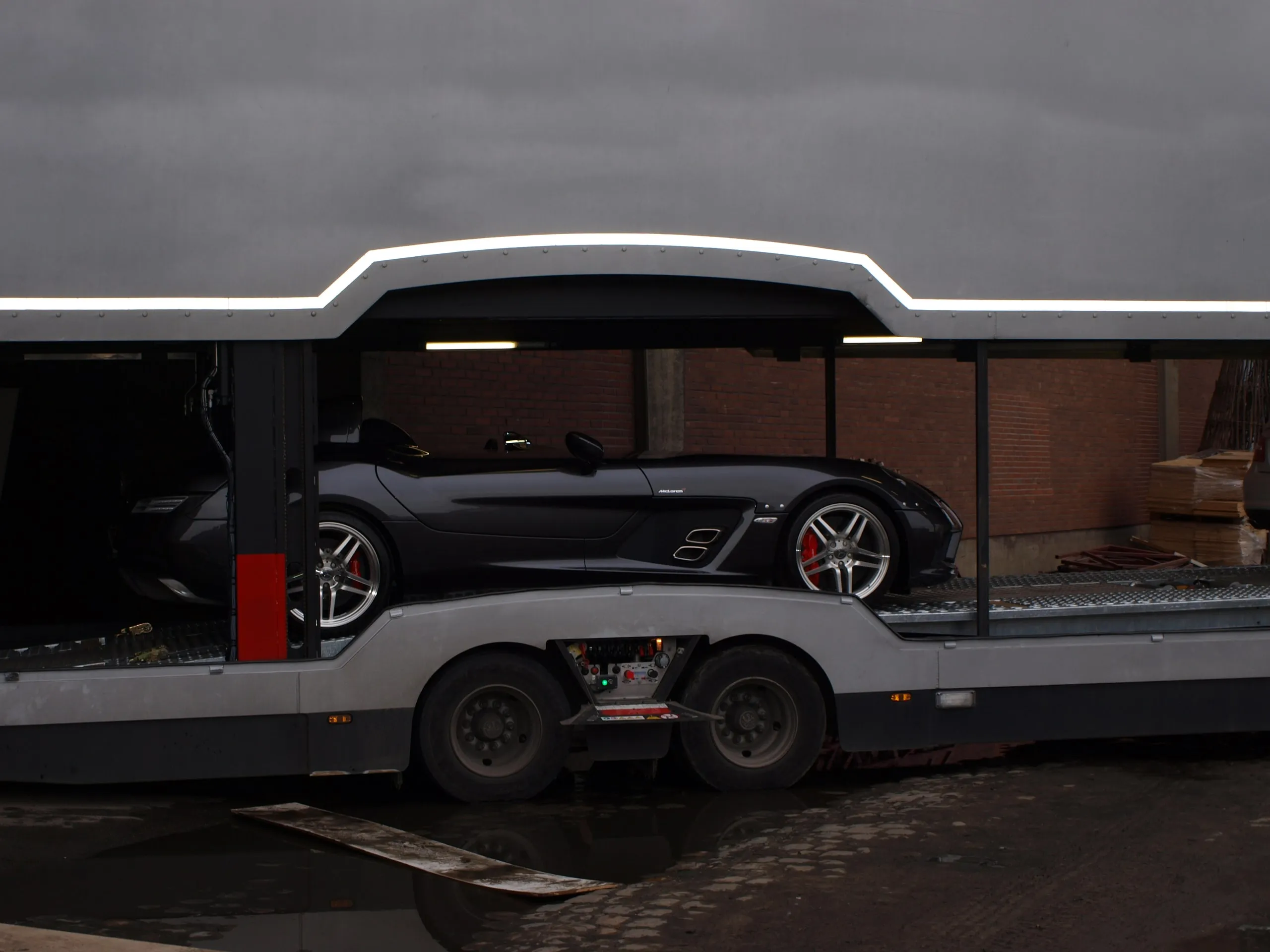 Mercedes SLR McLaren op het onderdek van een transporter naast een bakstenen loods