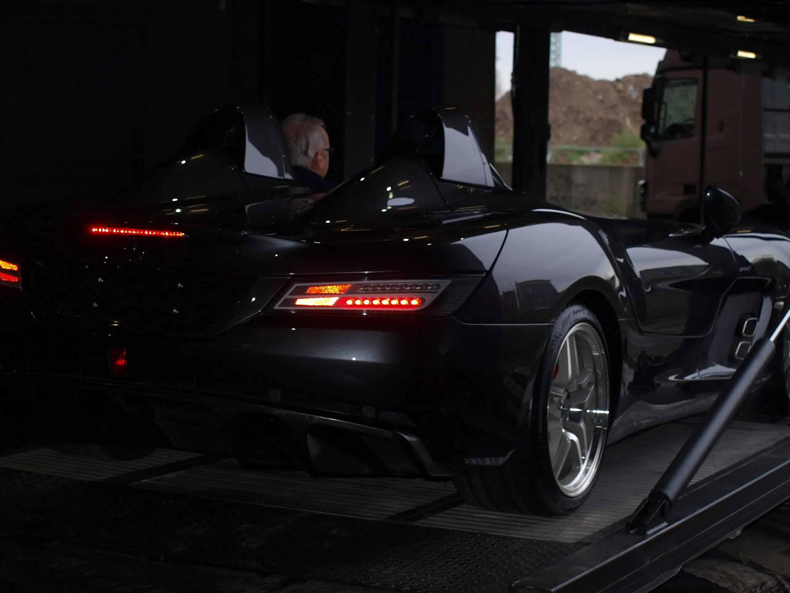 Achterzijde van een zwarte Mercedes SLR McLaren in een transporter, achterlichten aan