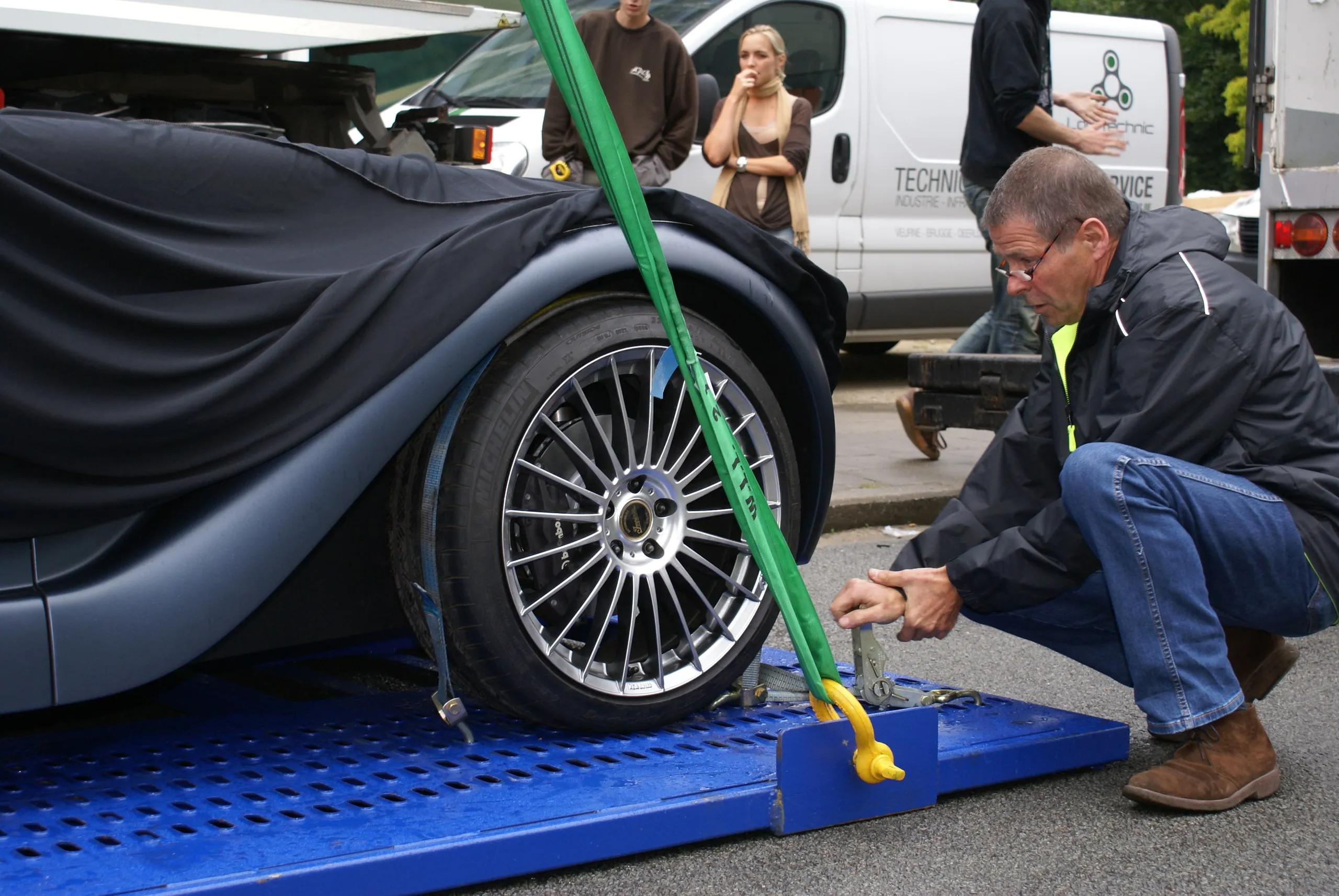 Crewlid spant een groene band op een afgedekte conceptcar voor de hijs