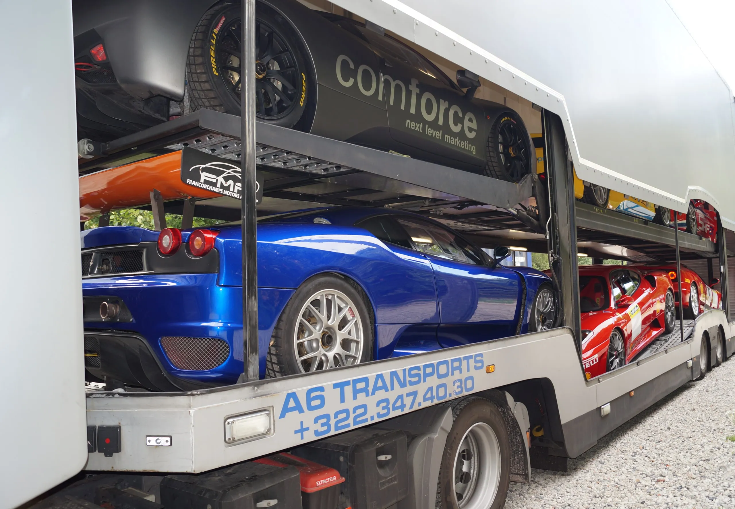 Blauwe en rode supercars op de dekken van een open transporter in bedrijfskleuren