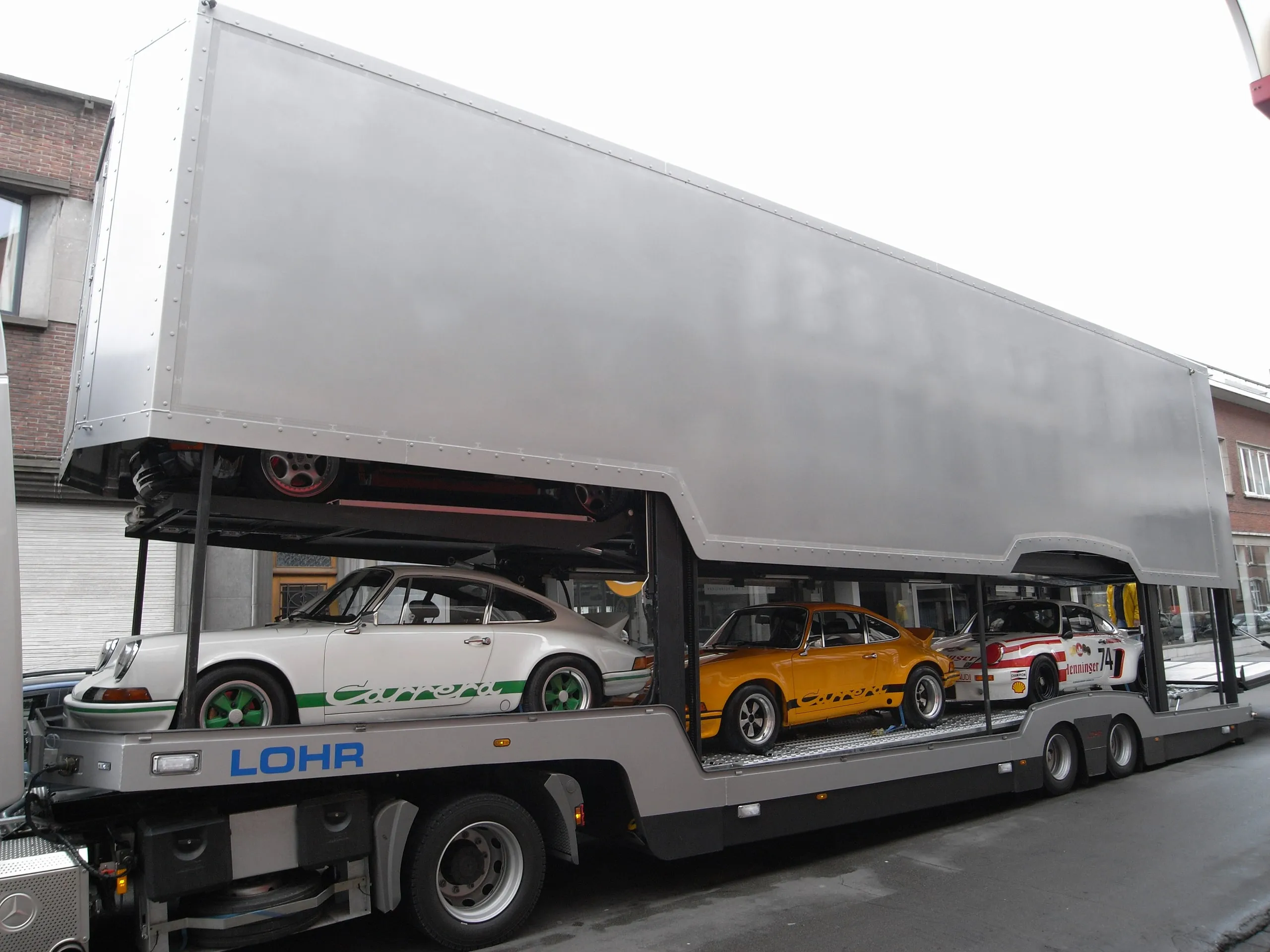 Mit mehreren Porsche 911 beladener Transporter hält in einer Dorfstraße